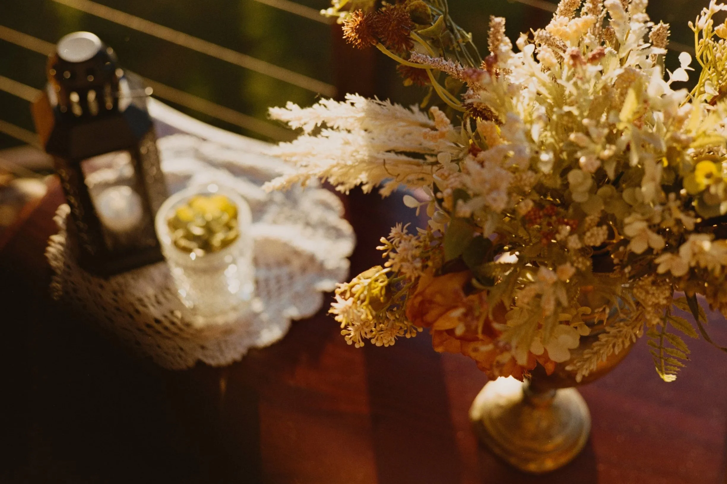 A detailed close-up of a bouquet of dried flowers in a vase, with a vintage style lamp and other decorative objects in the blurred background.