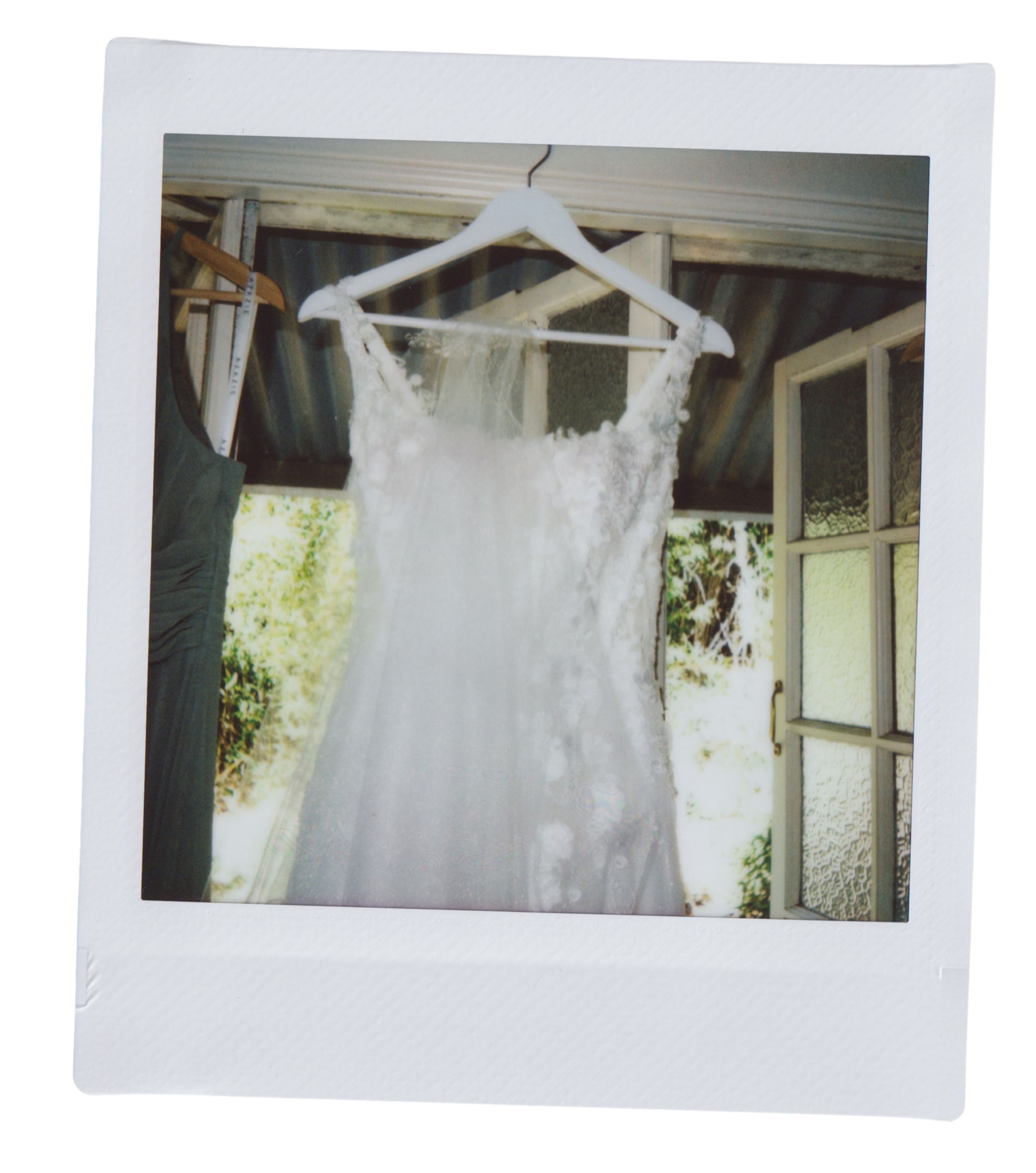 Photo of a wedding dress hanging on a white hanger, with a rustic porch and window visible in the background.
