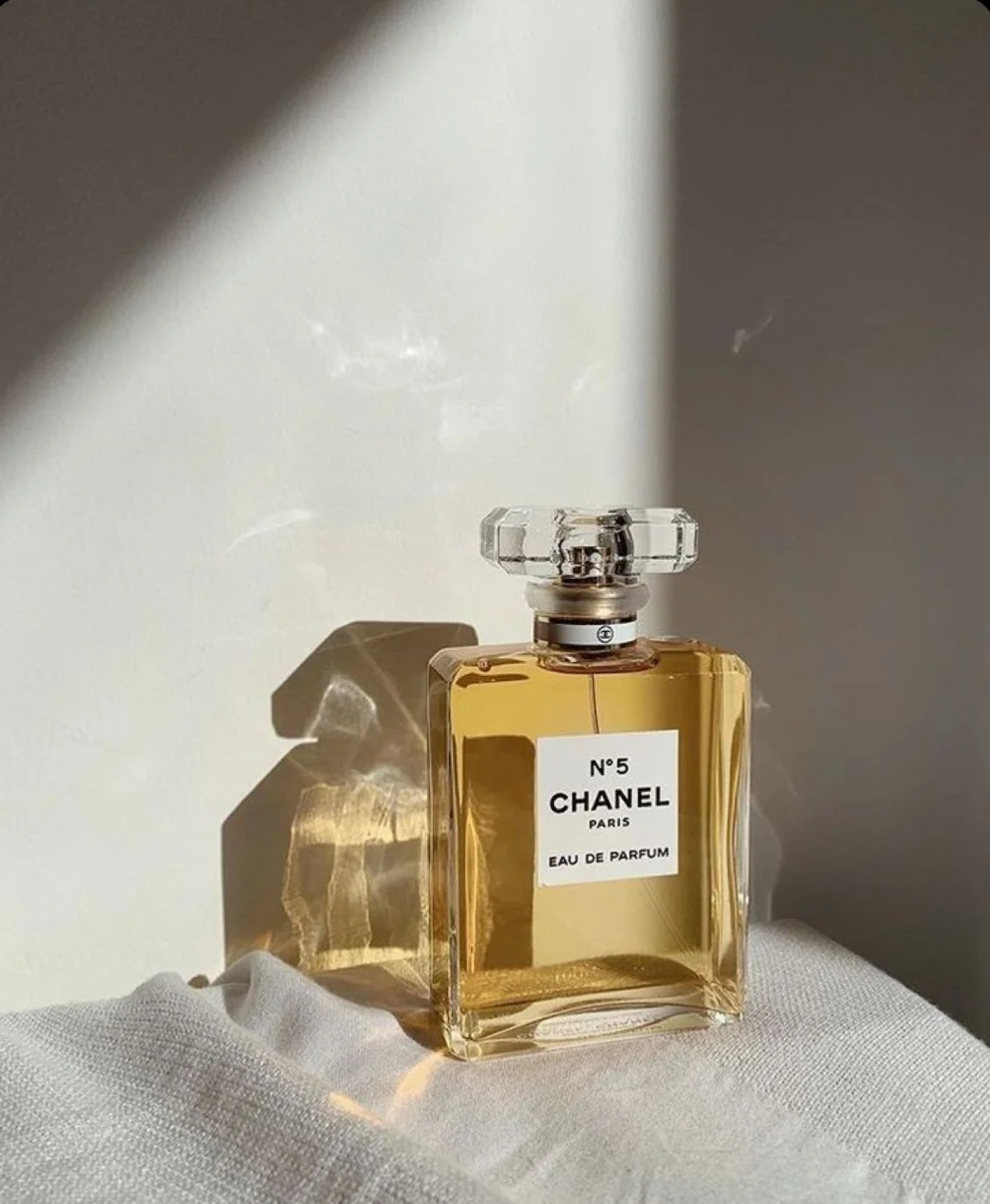A bottle of Chanel No. 5 Eau de Parfum sitting on a white fabric, with sunlight creating a shadow of the bottle on the wall.