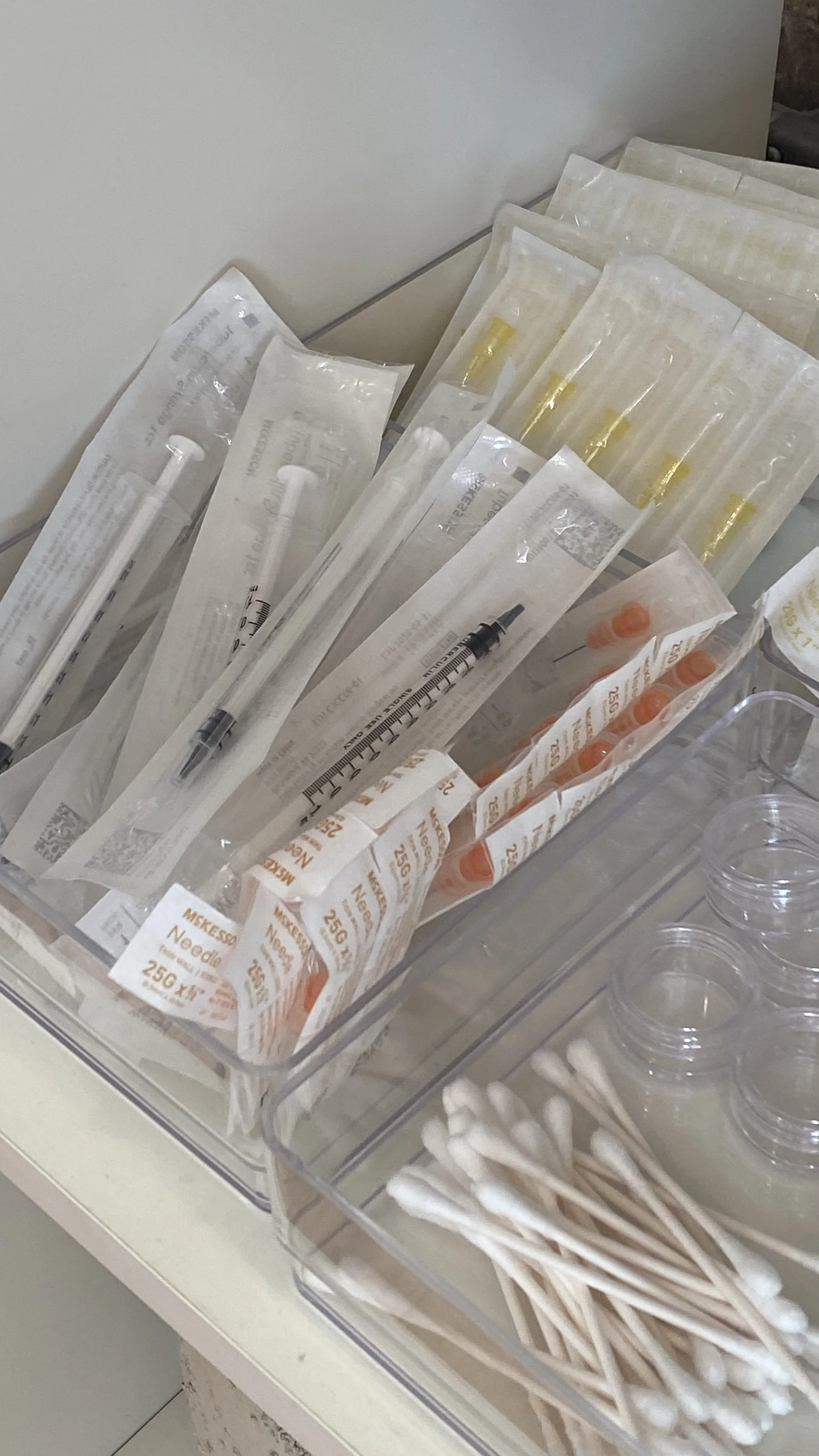 A medical supply tray with needles, syringes, and alcohol swabs, organized in clear containers.