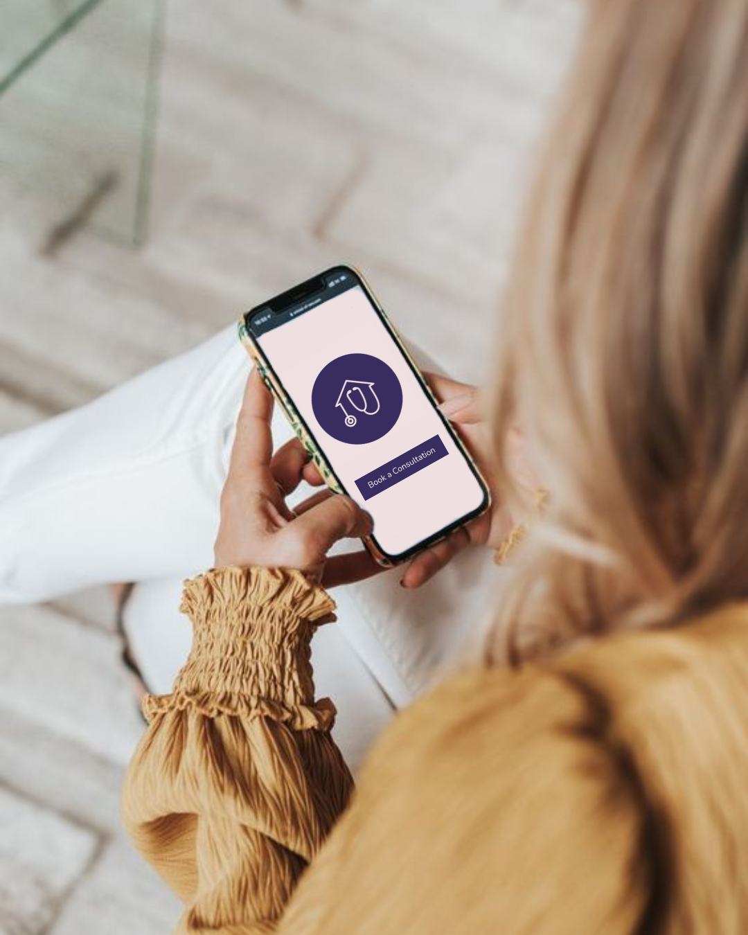 A woman holding a smartphone shows a website with a logo of a graduation cap and a stethoscope, and a button that says 'Book a Consultation'.