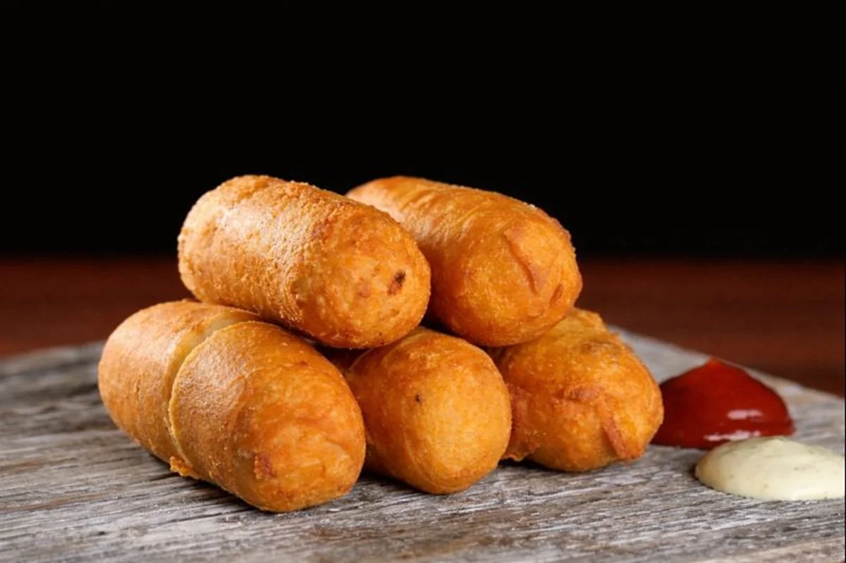 A stack of five tequenos on a wooden surface with ketchup and cilantro-garlic dipping sauces.