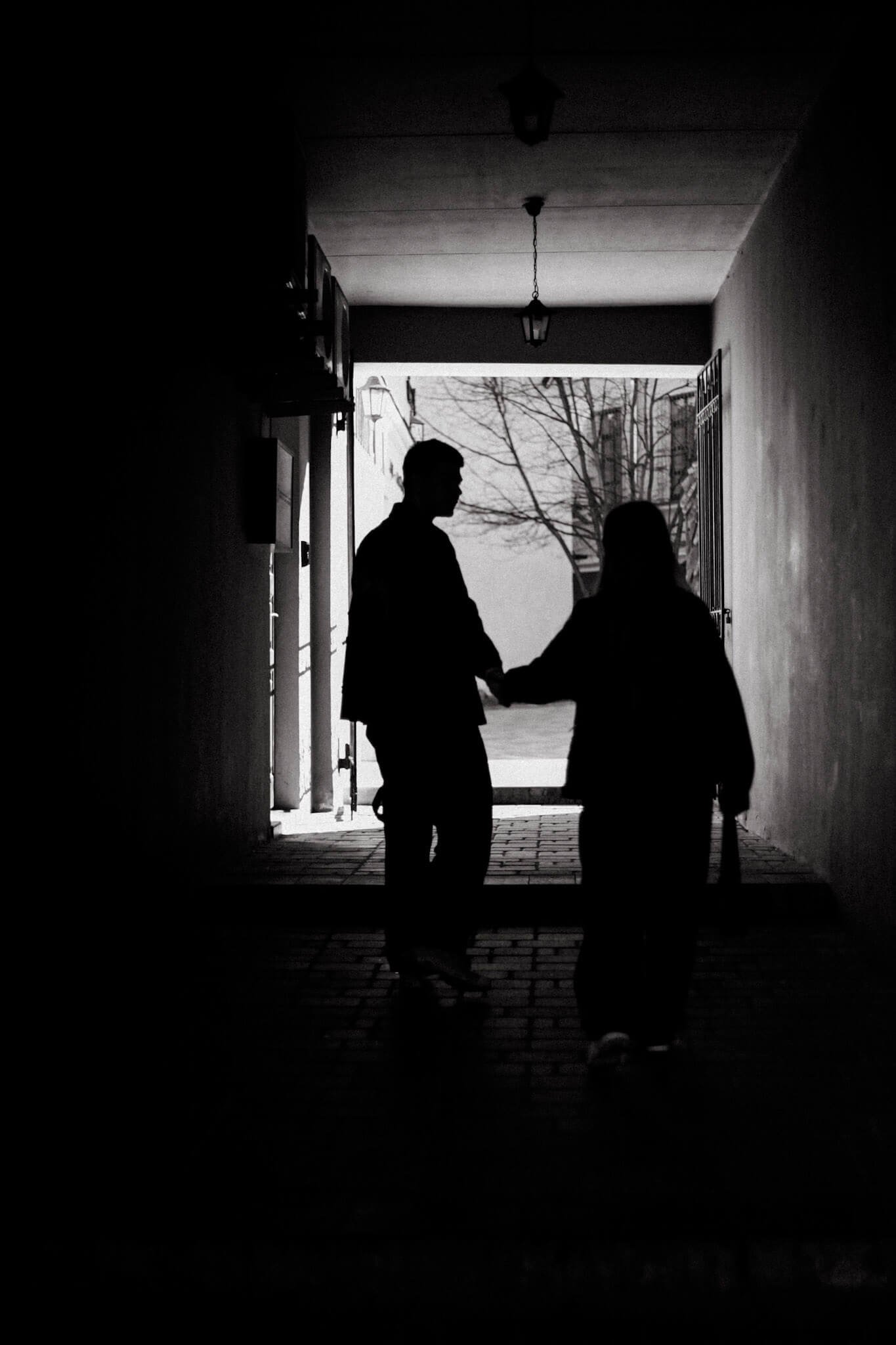 Silhouetted couple walking hand in hand through a stone corridor toward daylight