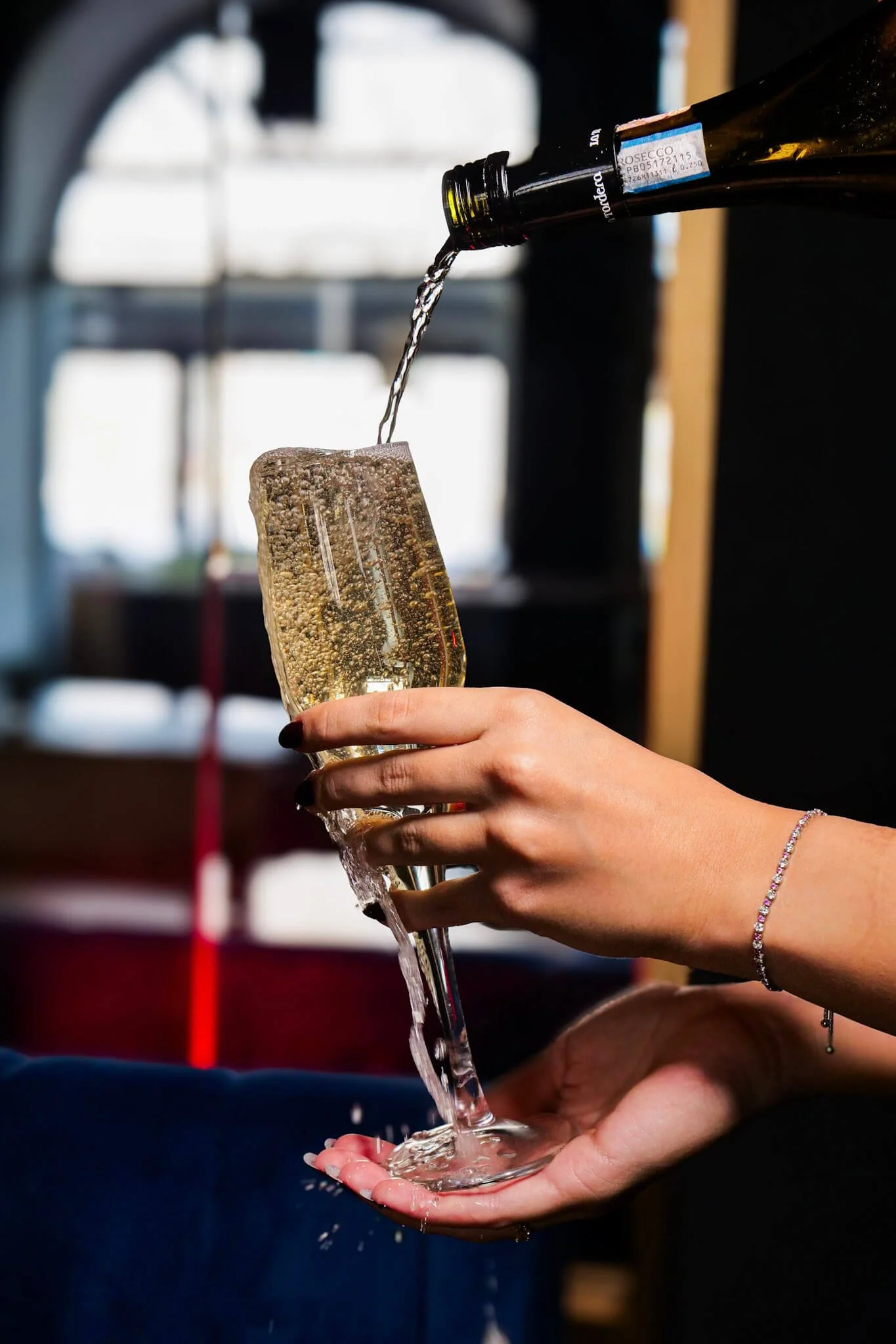 Champagne overflowing from a glass as it's poured, spilling over the hand holding it, warm ambient restaurant light in the background