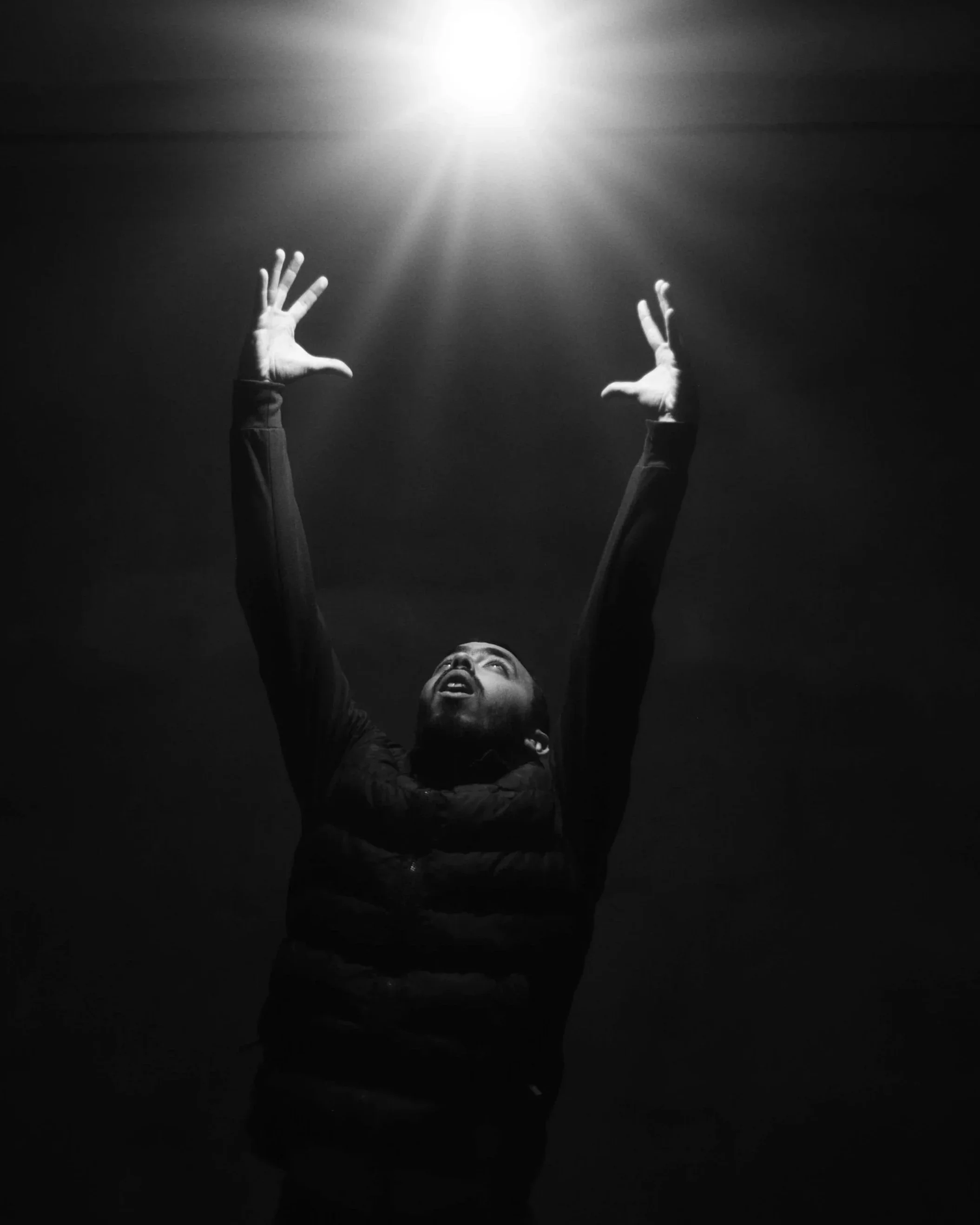 Black and white photo of a man standing with arms raised toward a bright beam of light in darkness, symbolizing spiritual revelation, accompanying Emanuel Swedenborg's quote on legacy and love from Heaven and Hell, 1758, on Words That Stay.