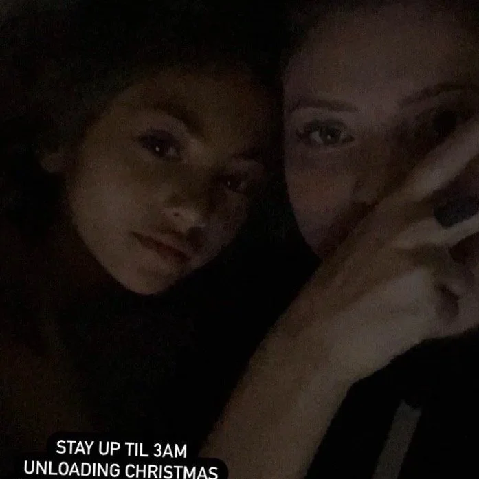 Two young women taking a selfie in a dark setting. One has her hand near her face, displaying a black nail. The photo has a caption that reads, 'STAY UP TIL 3AM UNLOADING CHRISTMAS.'