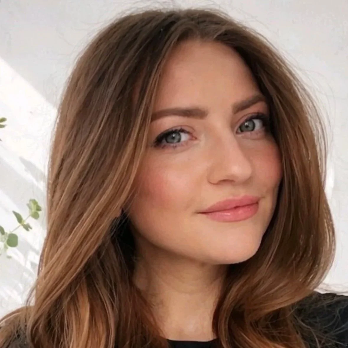 Close-up of a woman with long, wavy brown hair and blue eyes, smiling softly.