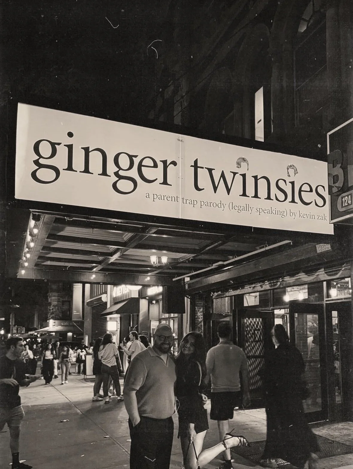 Black and white photo of a lively street scene at night outside a venue with a sign that reads "Ginger Twinsies: a parent trap parody (legally speaking) by Kevin Zak." People are standing and walking around, with some smiling and engaging in conversa