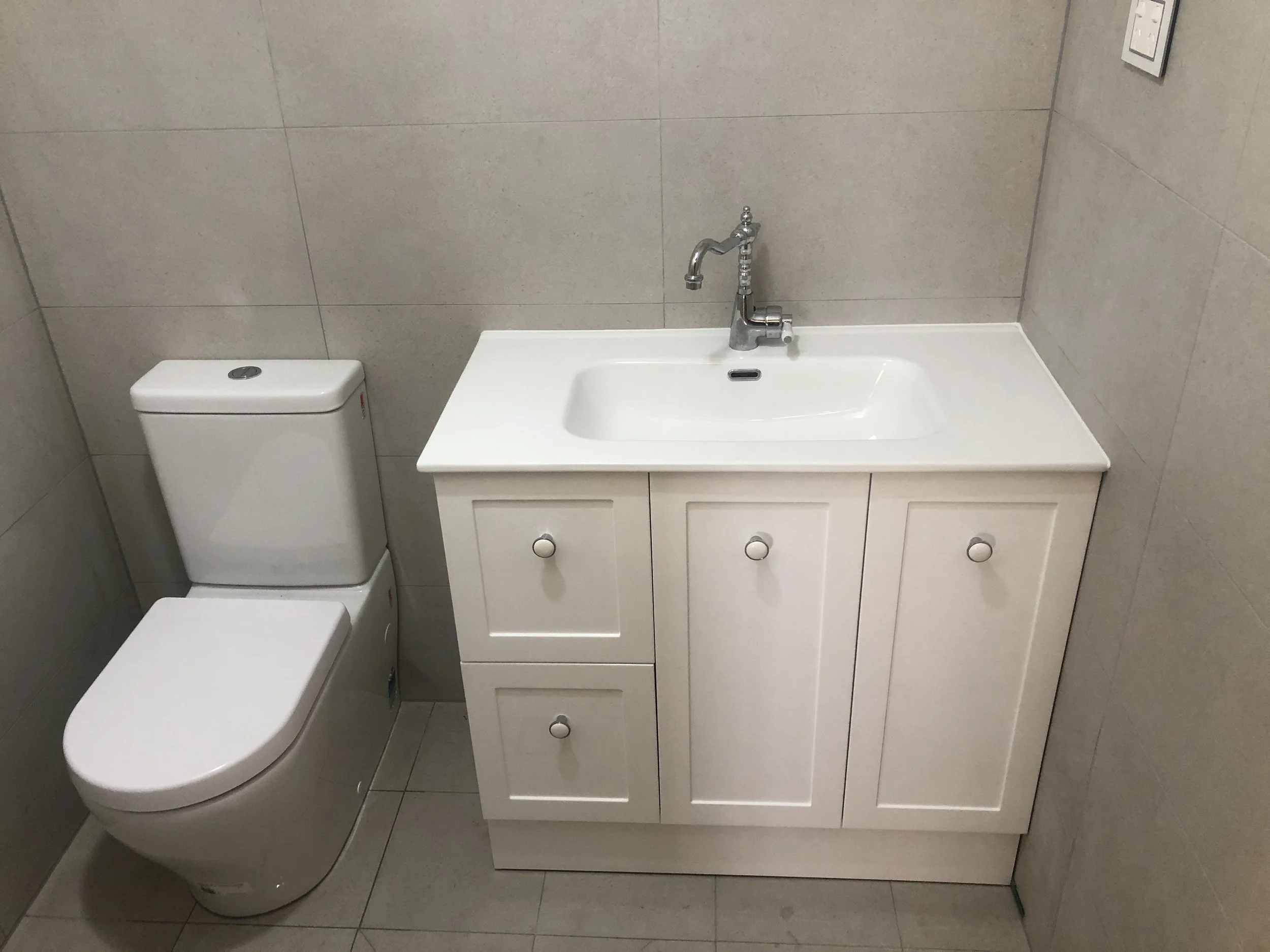 A bathroom with a white toilet and a white vanity with a sink and a faucet, all against tiled walls and floor.