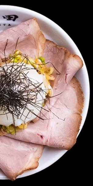 A bowl with slices of ham, a boiled egg, shredded lettuce, and garnish with black shredded seaweed.