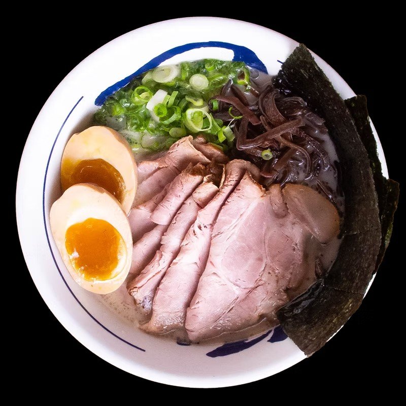 A bowl of ramen noodles topped with sliced pork, soft-boiled eggs, green onions, seaweed, and black mushrooms.