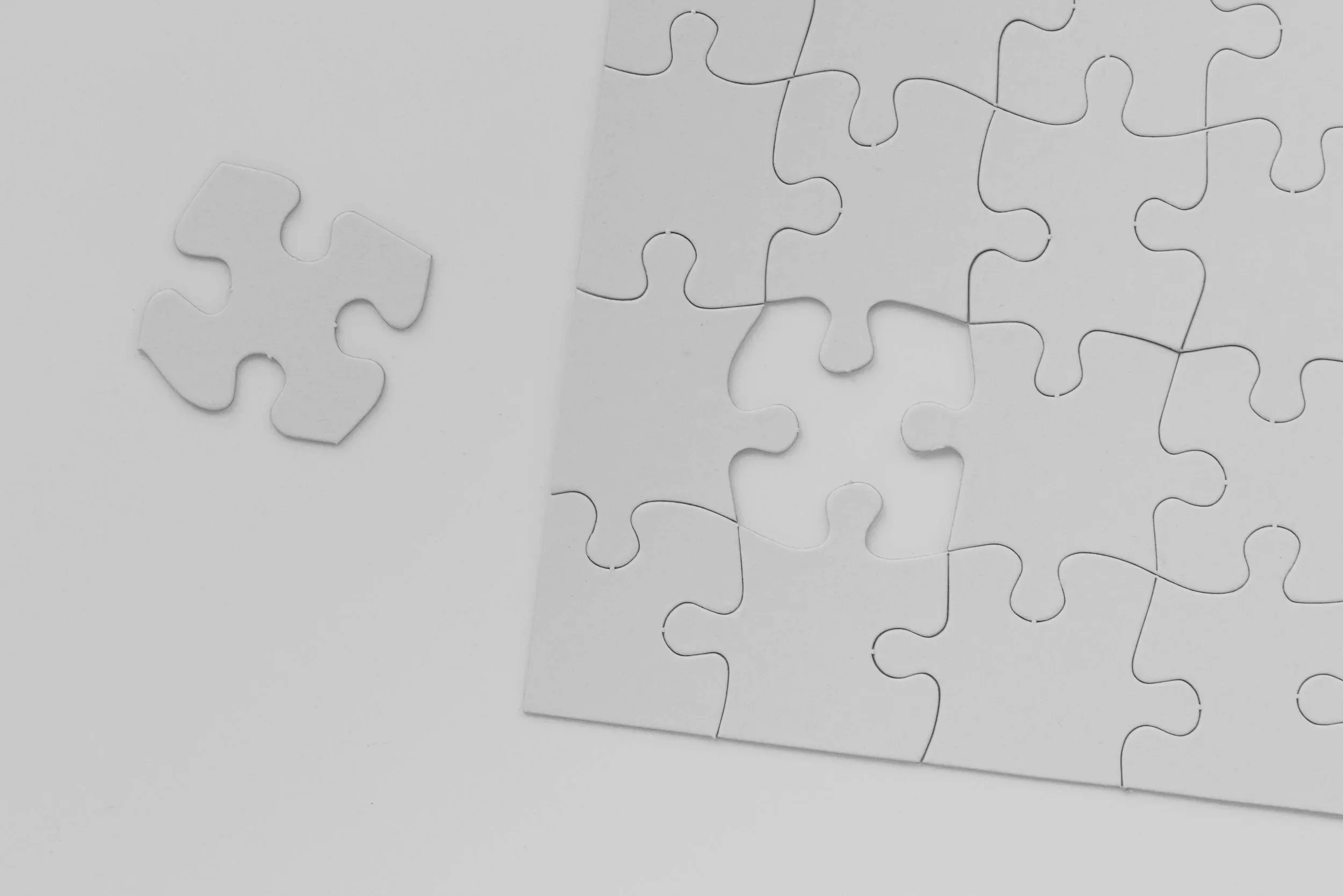 Several plain white puzzle pieces, some connected and some separated, on a light background.