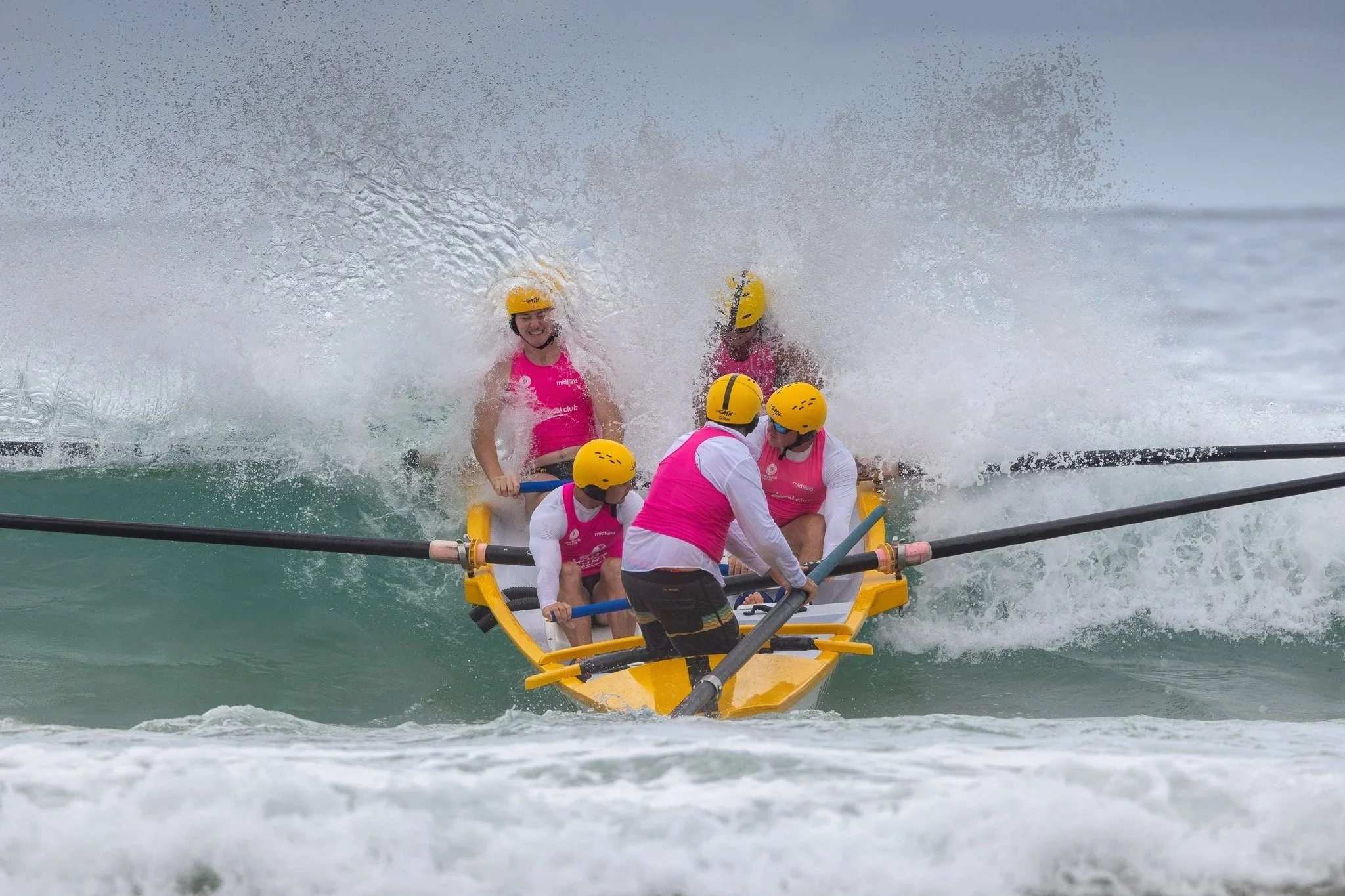 A group of people in pink shirts and yellow helmets riding a yellow raft, navigating through white water rapids on a river.