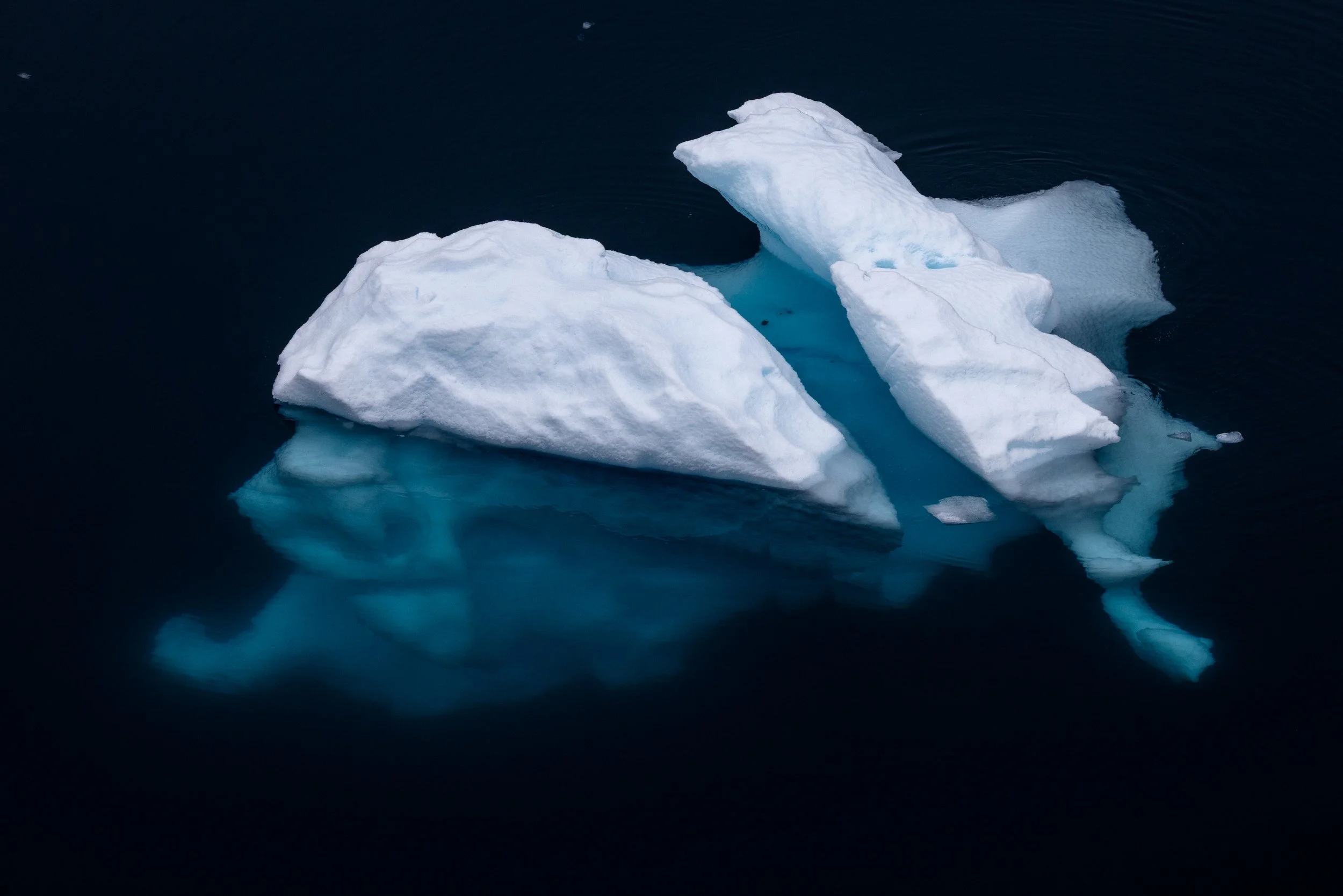 An iceberg floating in dark water, showing its white icy surface and blue interior.