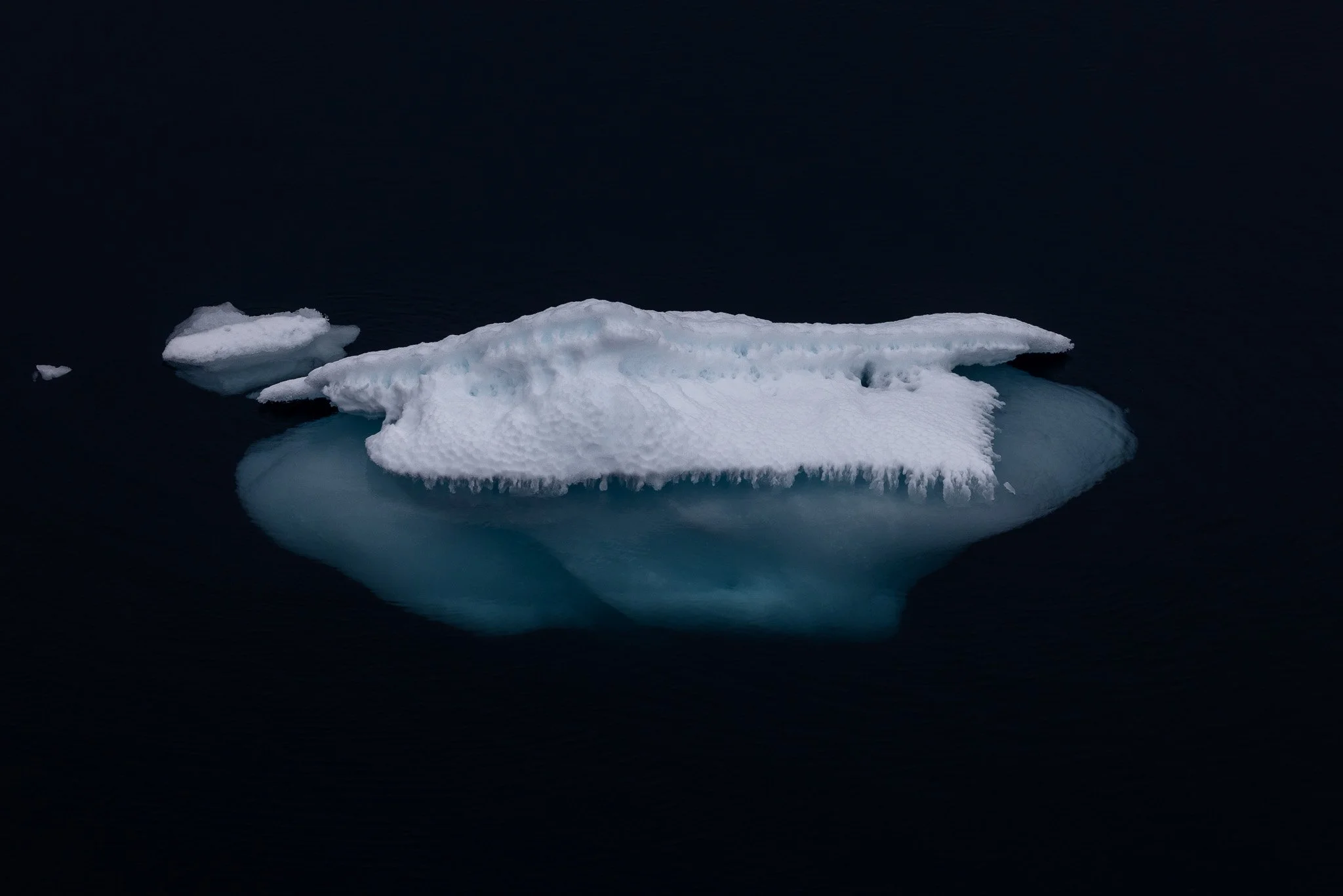 A large iceberg floating in dark water, with a reflection visible beneath.
