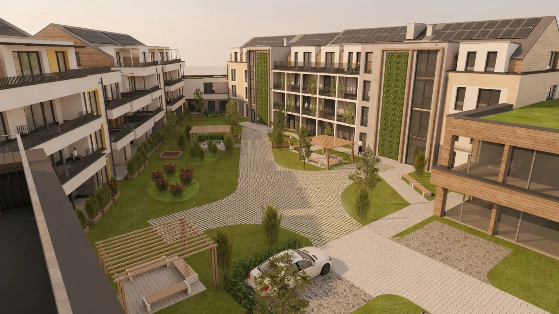 Ein moderner Innenhof eines Wohnkomplexes mit Grünflächen, Bänken, kleinen Bäumen und einem Pkw. Mehrstöckige Gebäude mit Balkonen umgeben den Hof, einige Bewohner sind zu sehen.