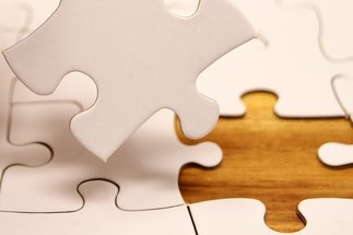 Close-up of disassembled white jigsaw puzzle with one piece removed on a wooden surface