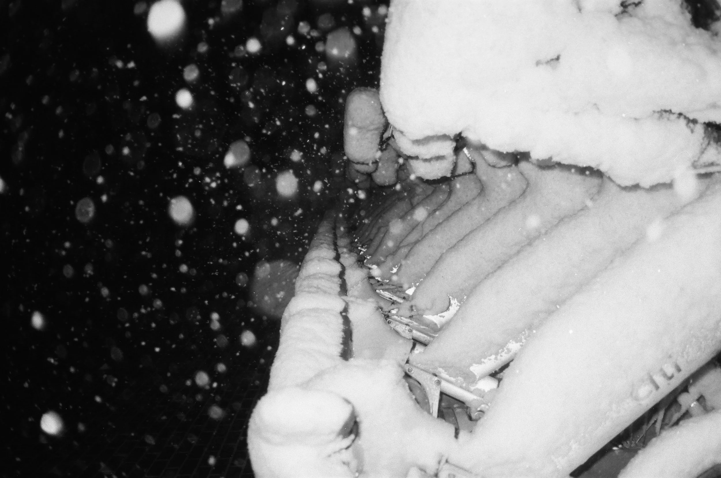 Snow-covered backyard with a swing set and snow-covered trees in the background at night, with snow falling.