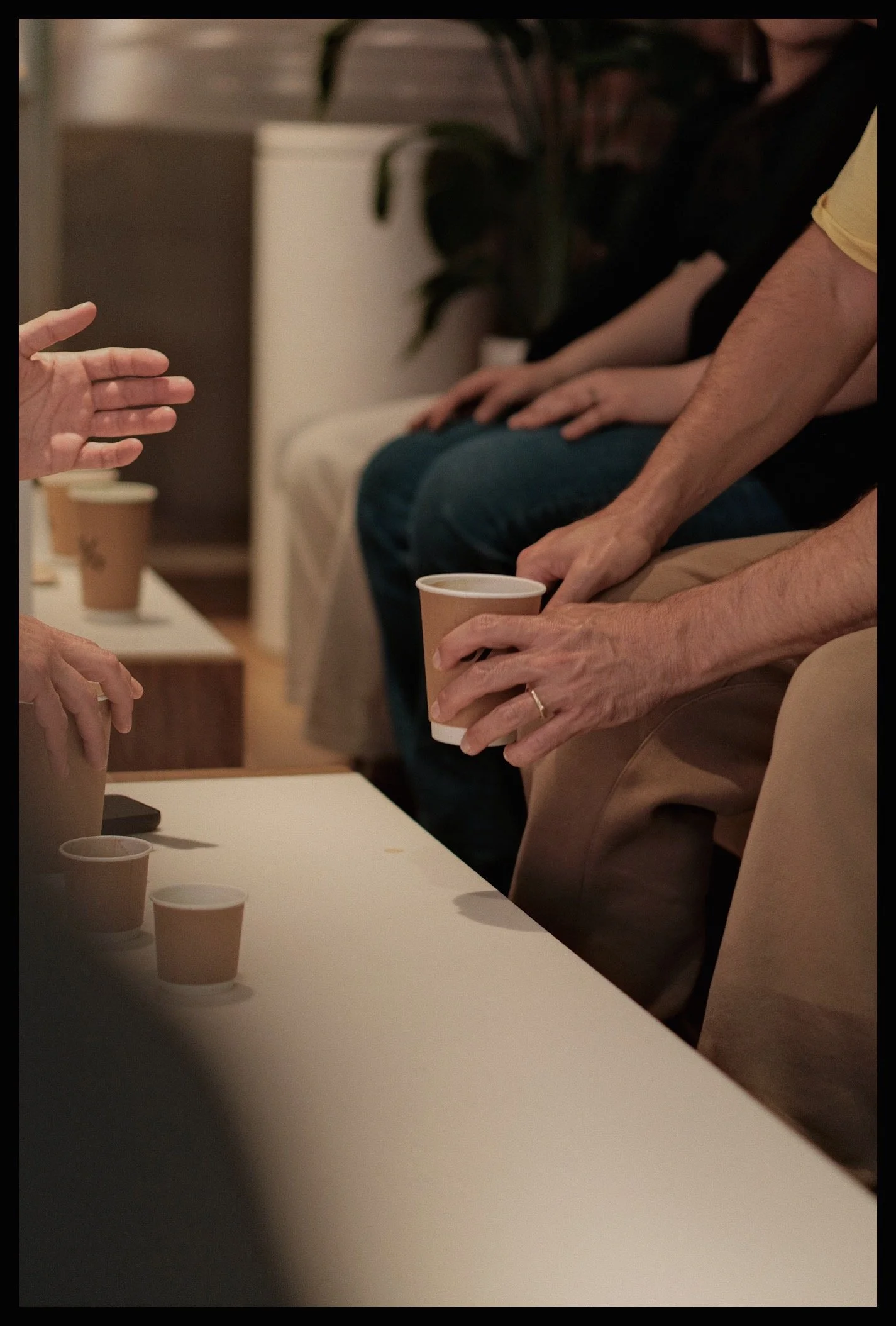 People seated at a table during a social gathering, with hands reaching for cups of coffee or tea.