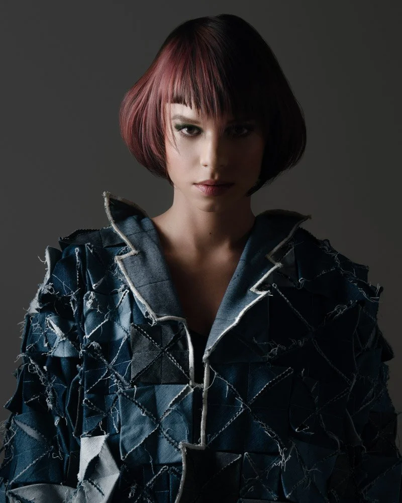 A woman with short, multicolored hair wearing a textured, patchwork-style jacket.