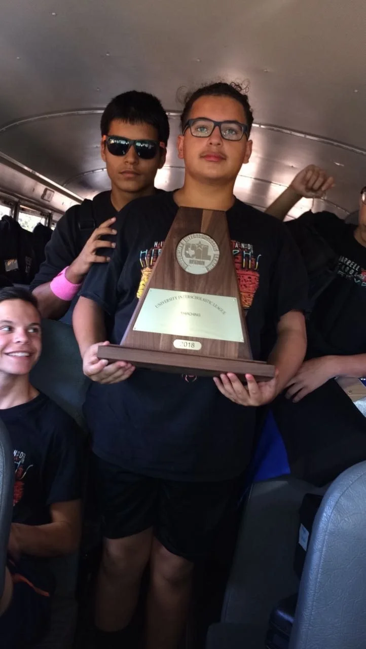 Two boys on a bus with one holding a trophy, celebrating their achievement in a science or academic competition.