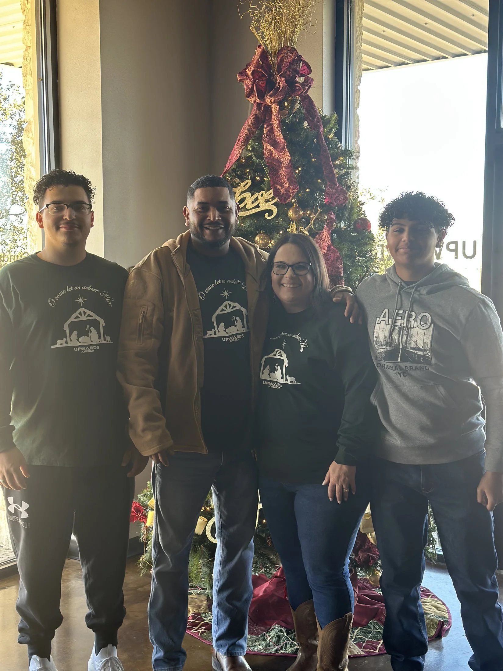 Four people standing in front of a decorated Christmas tree inside a building, smiling at the camera.