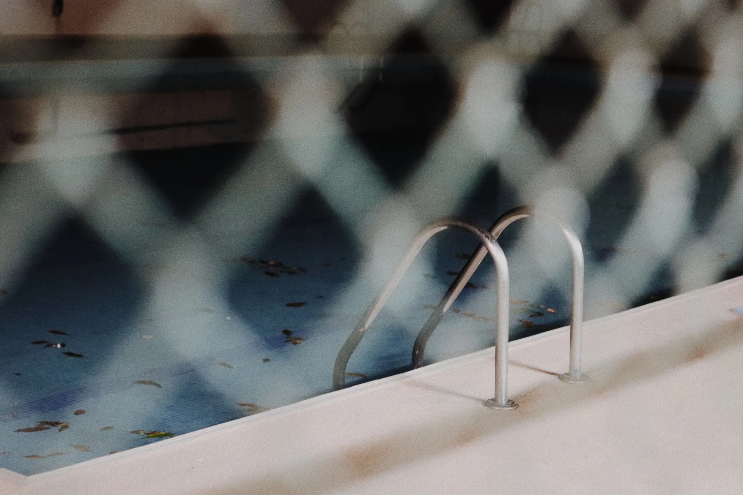 Close-up of a pool or baby pool with a metal ladder, water, and floating leaves.