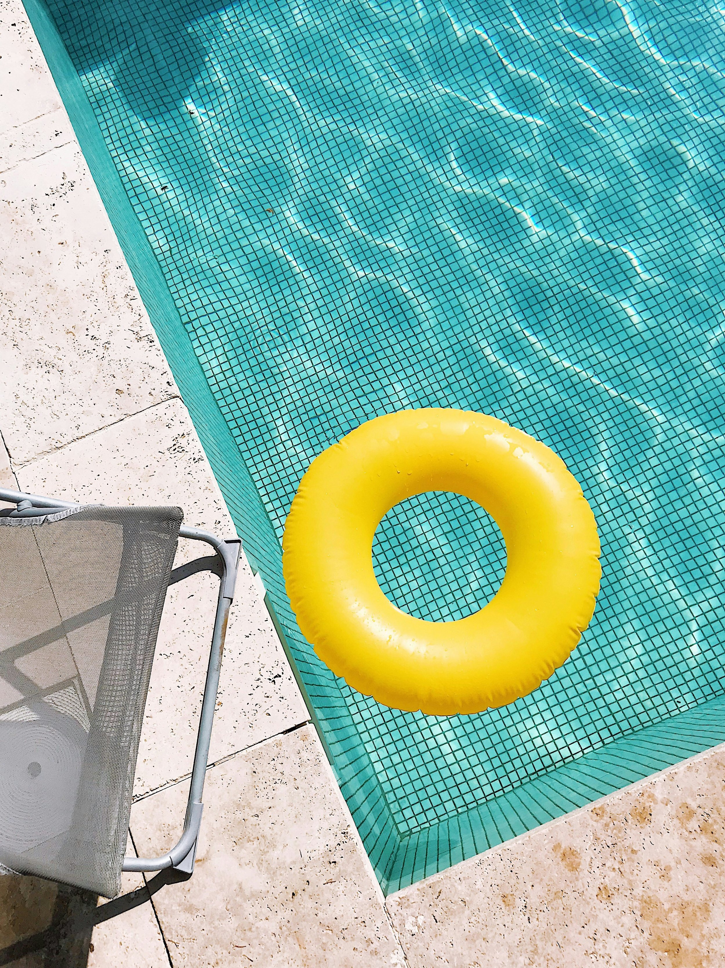 Swimming pool with turquoise tiles and a yellow pool float. There is a lounge chair and a white tiled pool deck.