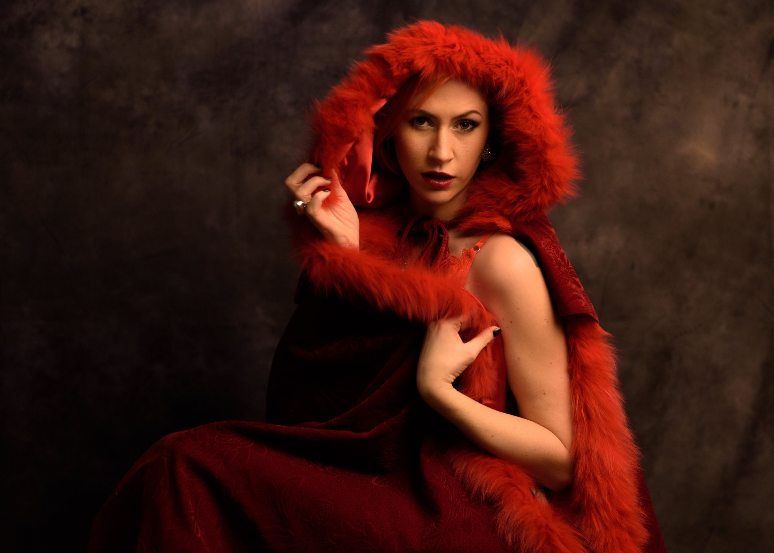 A woman with red hair and makeup wearing a red hooded fur coat.