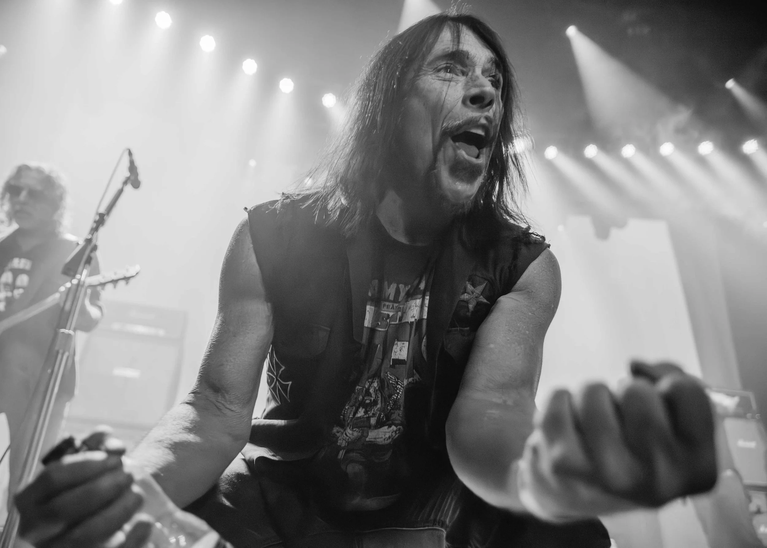Monster Magnet - Shot by Shotison. A black-and-white photo of a long-haired male guitarist passionately playing on stage with an expressive facial expression, illuminated by stage lights, with another musician visible in the background.