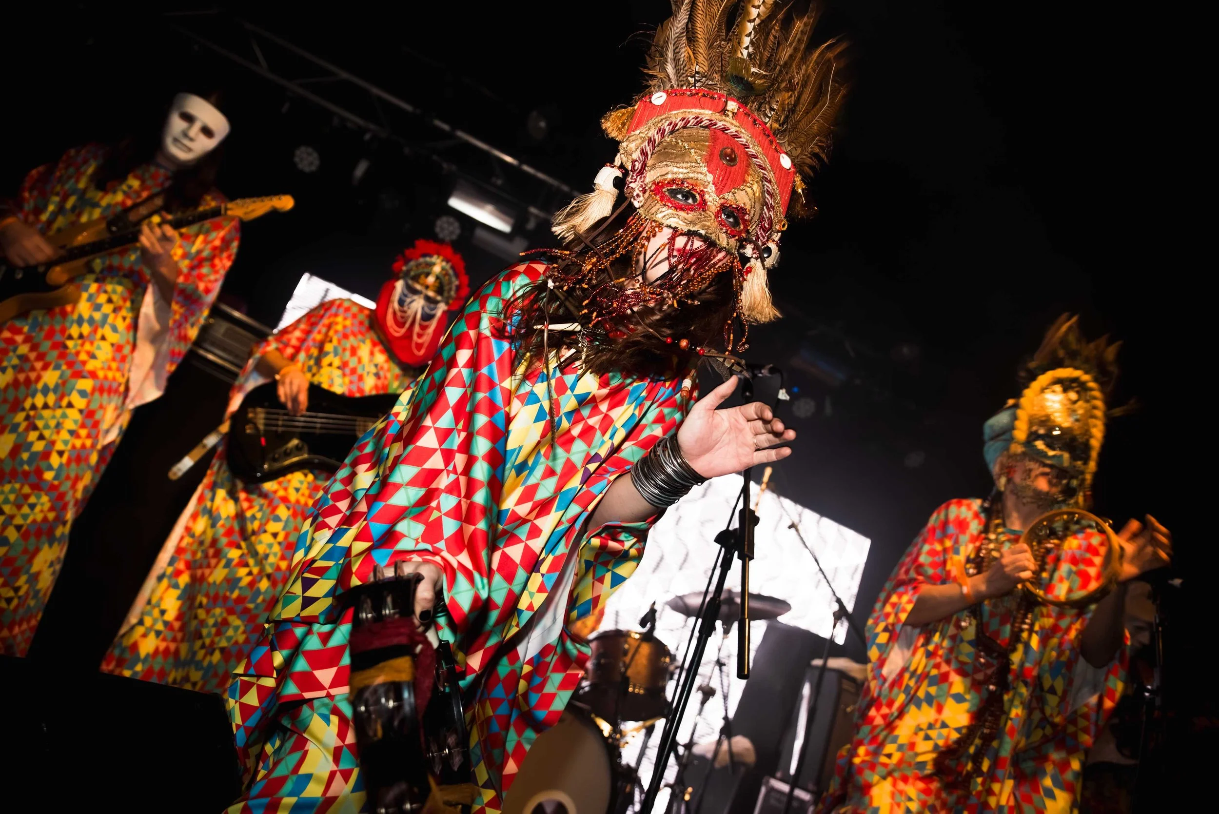 Goat - Shot by Shotison. People in colourful, geometric-patterned costumes and masks performing on stage with musical instruments at a cultural event.