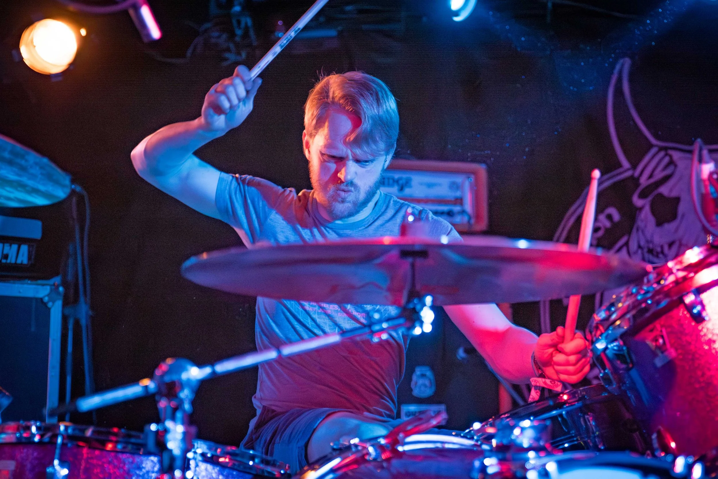 A man with blond hair playing drums on stage with colorful lighting.