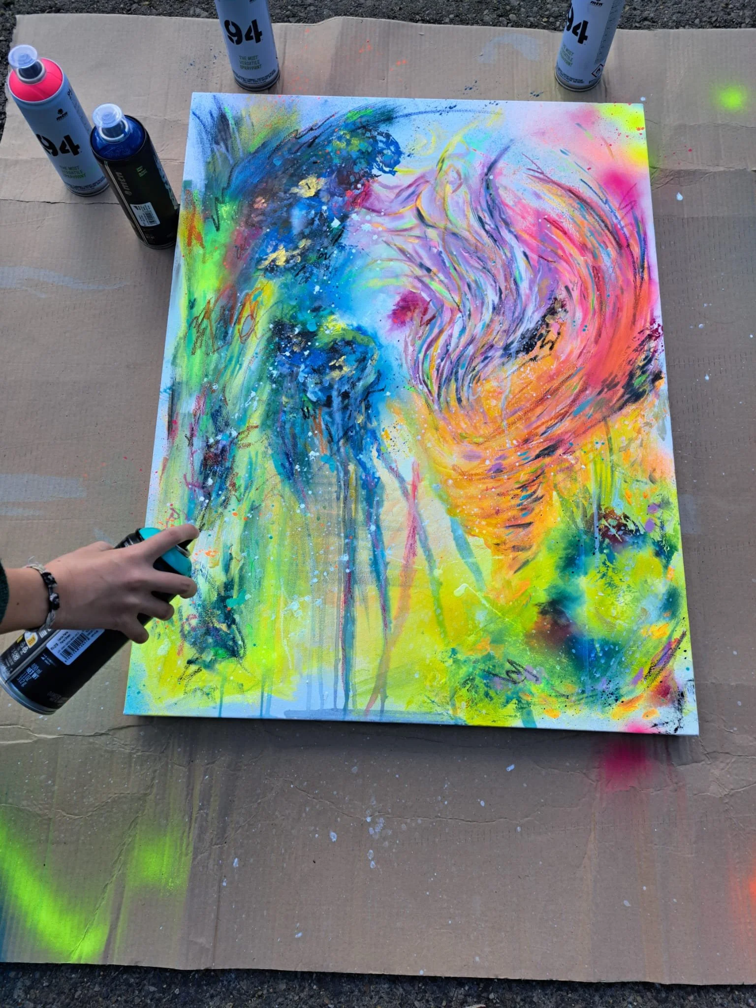 Pintura abstracta con colores brillantes y vibrantes, con sprays y manchas dispersas sobre el papel, enmarcada por una mesa de cartón y spray pintados alrededor.