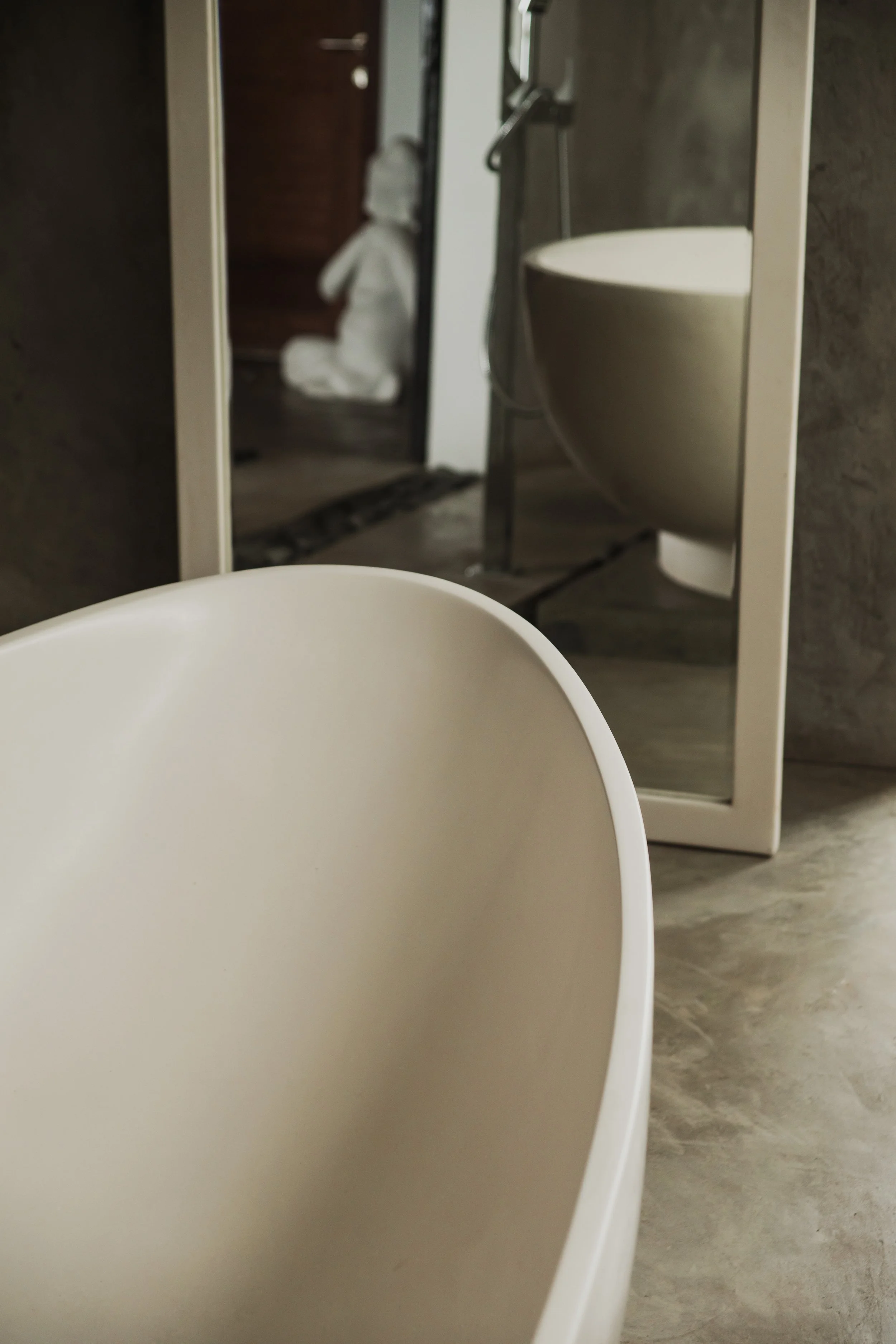 Part of a white chair or table in the foreground, with a bathroom mirror reflecting a sink, mirror, and towel in the background.