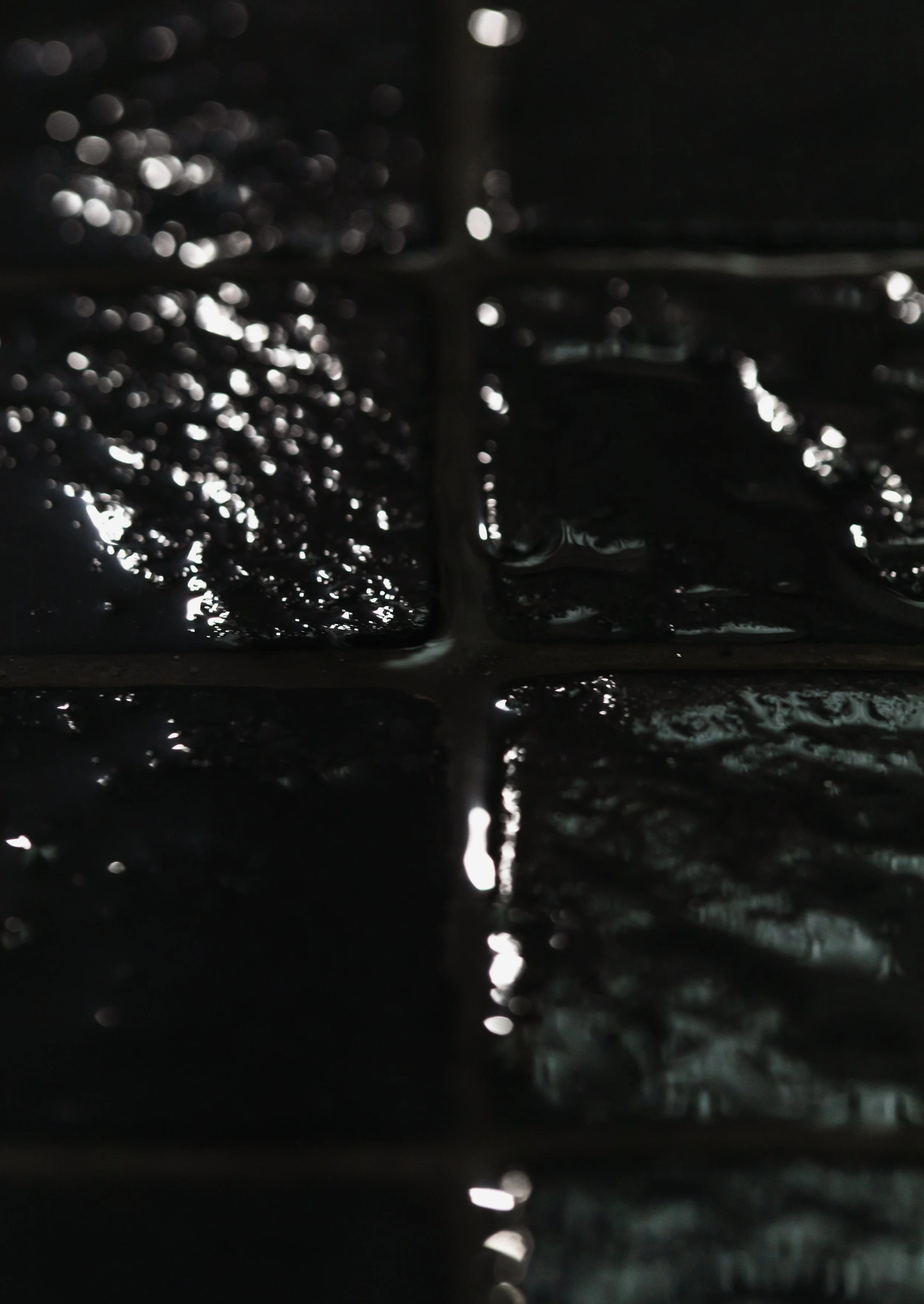 Close-up of a wet surface with water droplets and reflections in a dark environment.