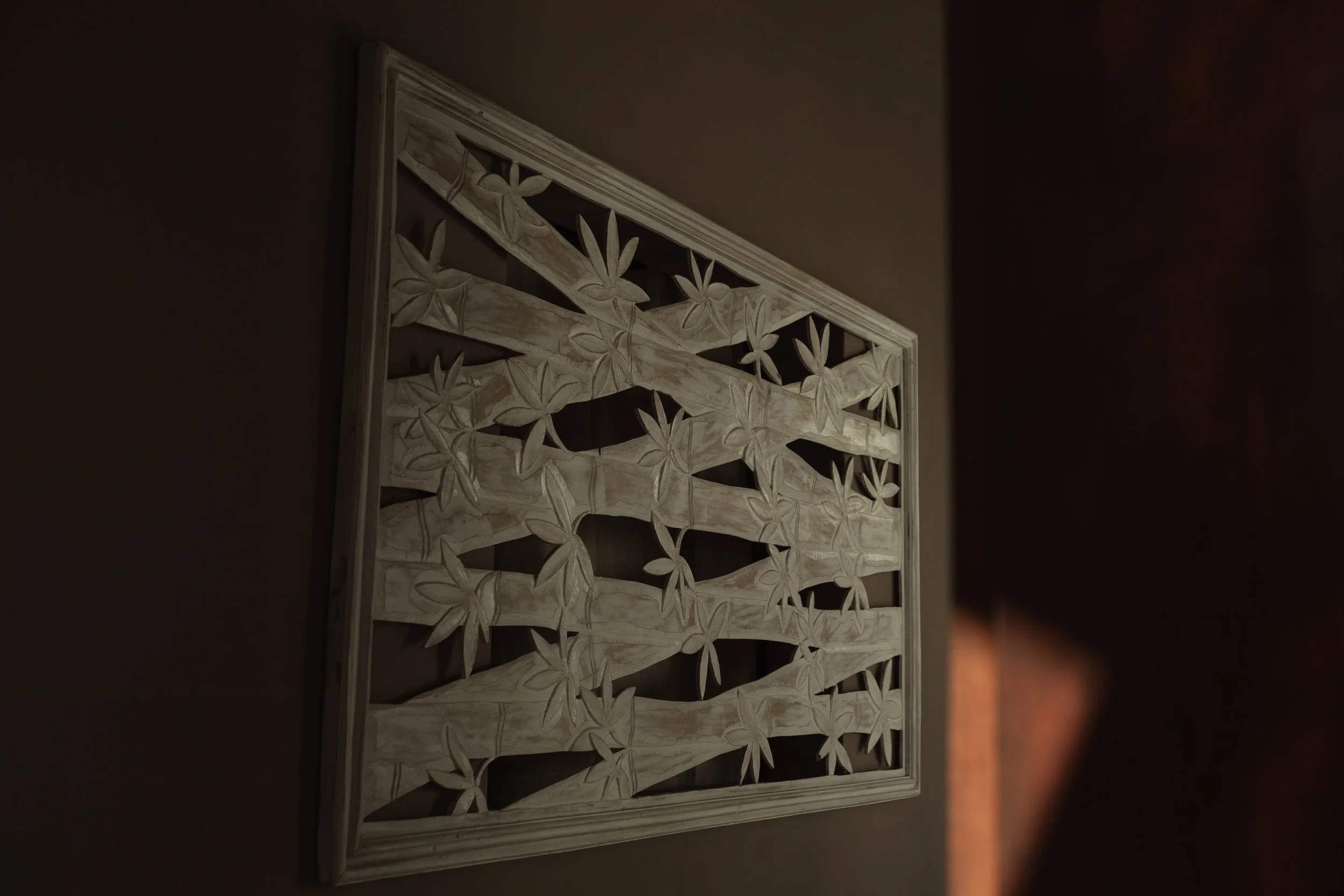 A framed carved wooden wall art piece with a floral pattern, placed on a dark wall.