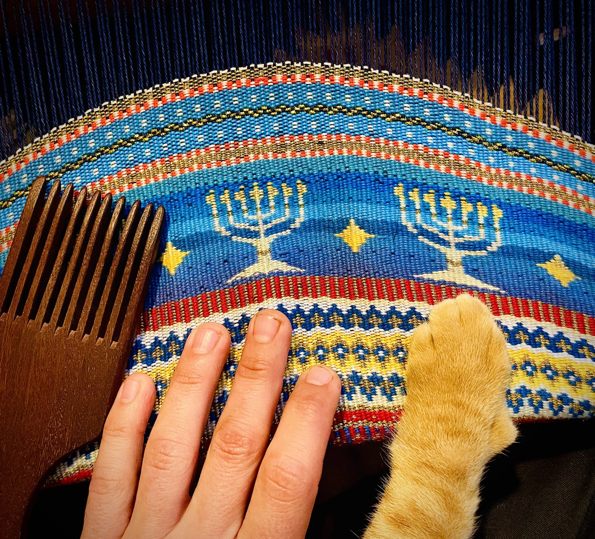 Close-up of a colorful, embroidered fabric with a rainbow and menorah design, held by a person's fingers. weaving. craft by Avi Mazliah clothes and costumes, 