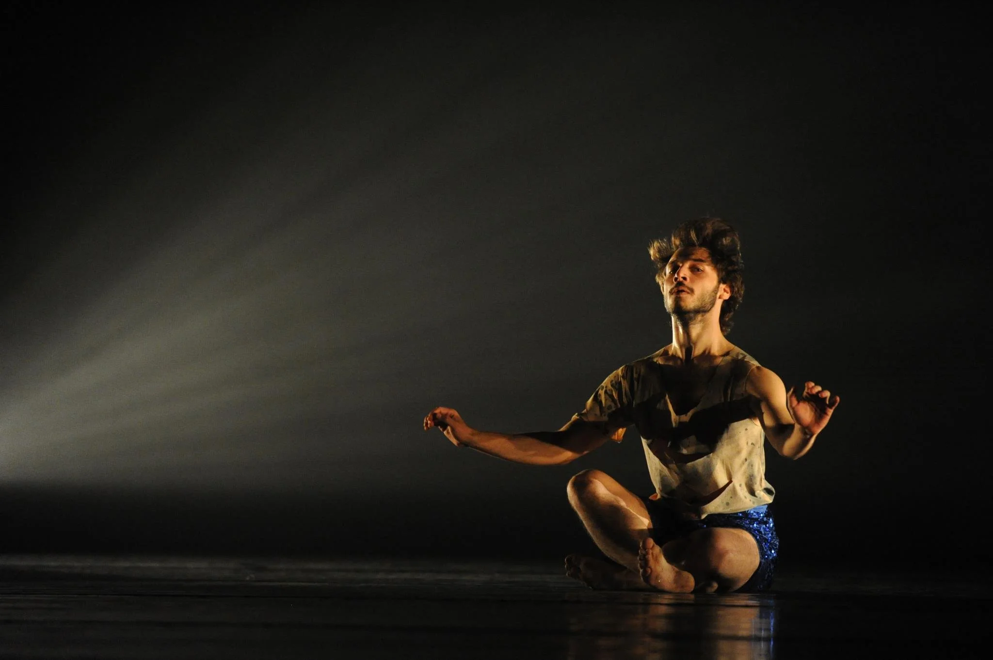 A person performing a dance move on a dark stage, illuminated by stage lighting, with a black background. Avi Mazliah, dance ,dancing, performance