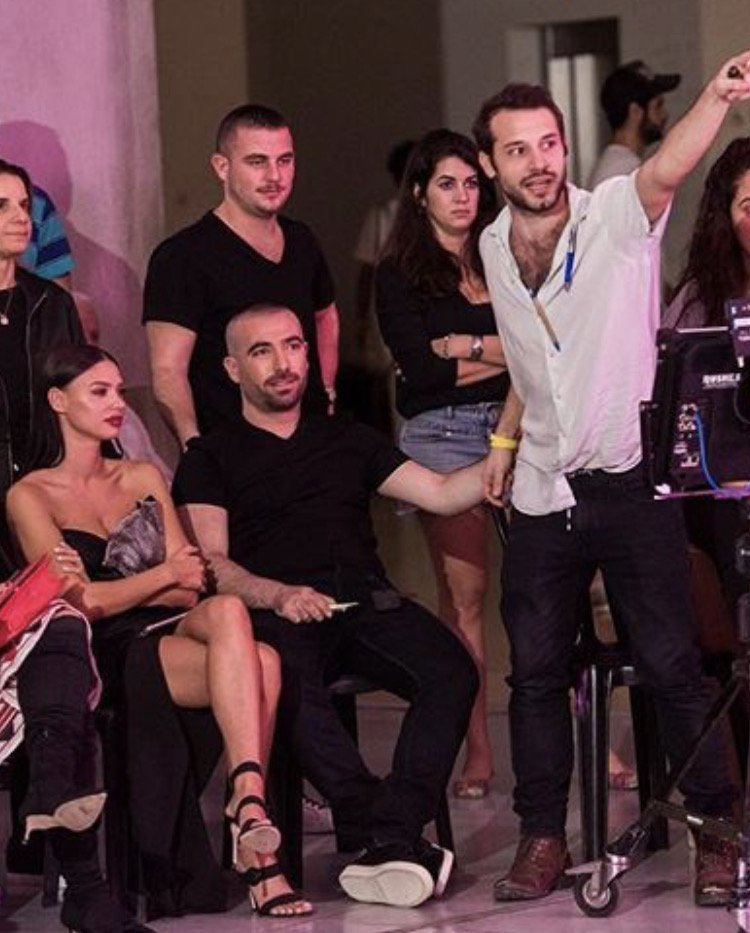 A group of people, including a woman in a black strapless dress and a man in black , a film set or event.  a camera , monitor, . Omer Adam Music Video Behind the seance, music video director 