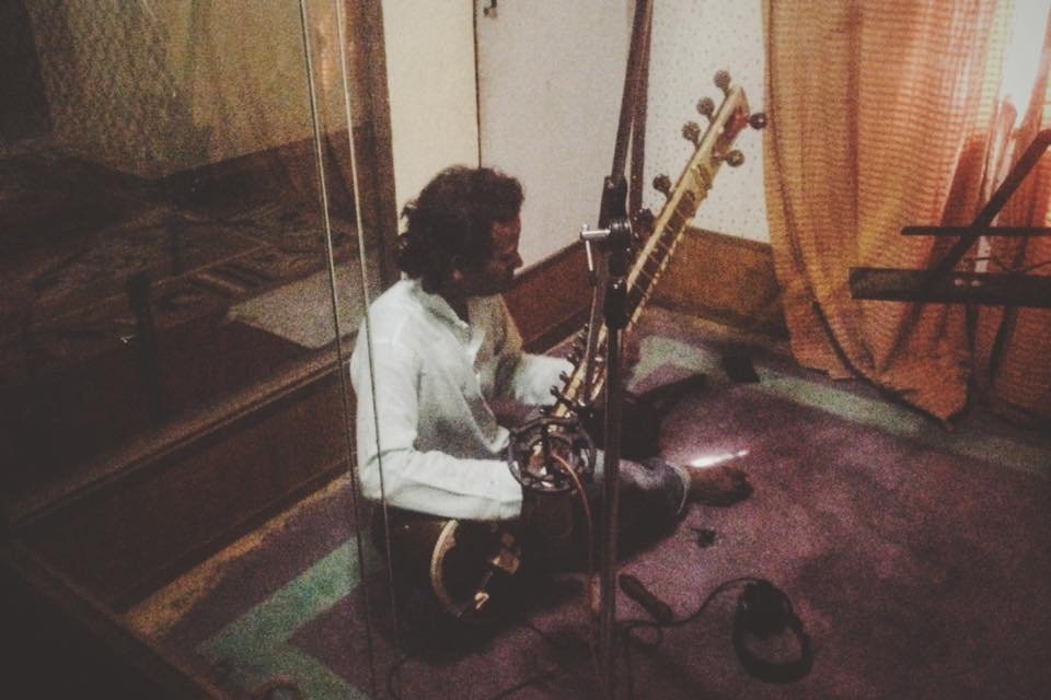 A man sitting on the floor playing an sitar in a recording studio.