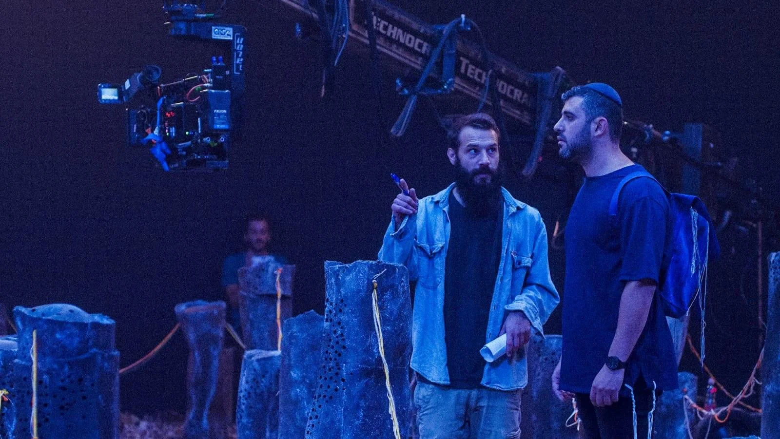 Two men having a conversation on a film set with professional filming equipment and large black backgrounds. music video director , Music video clip