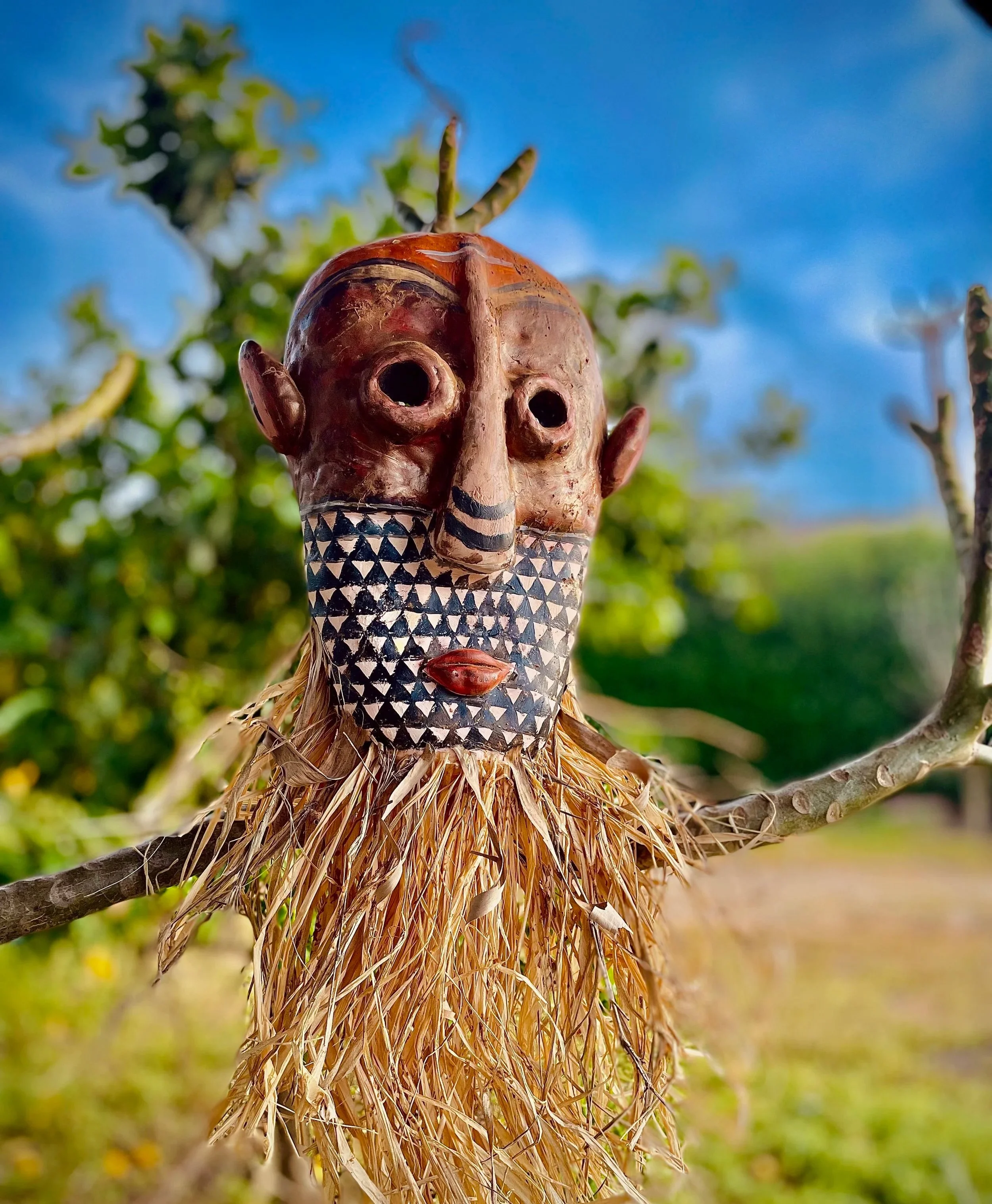 A wooden carved figure with an elongated nose, hollow eyes, and geometric painted facial features. African mask, craft by Avi Mazliah clothes and costumes
