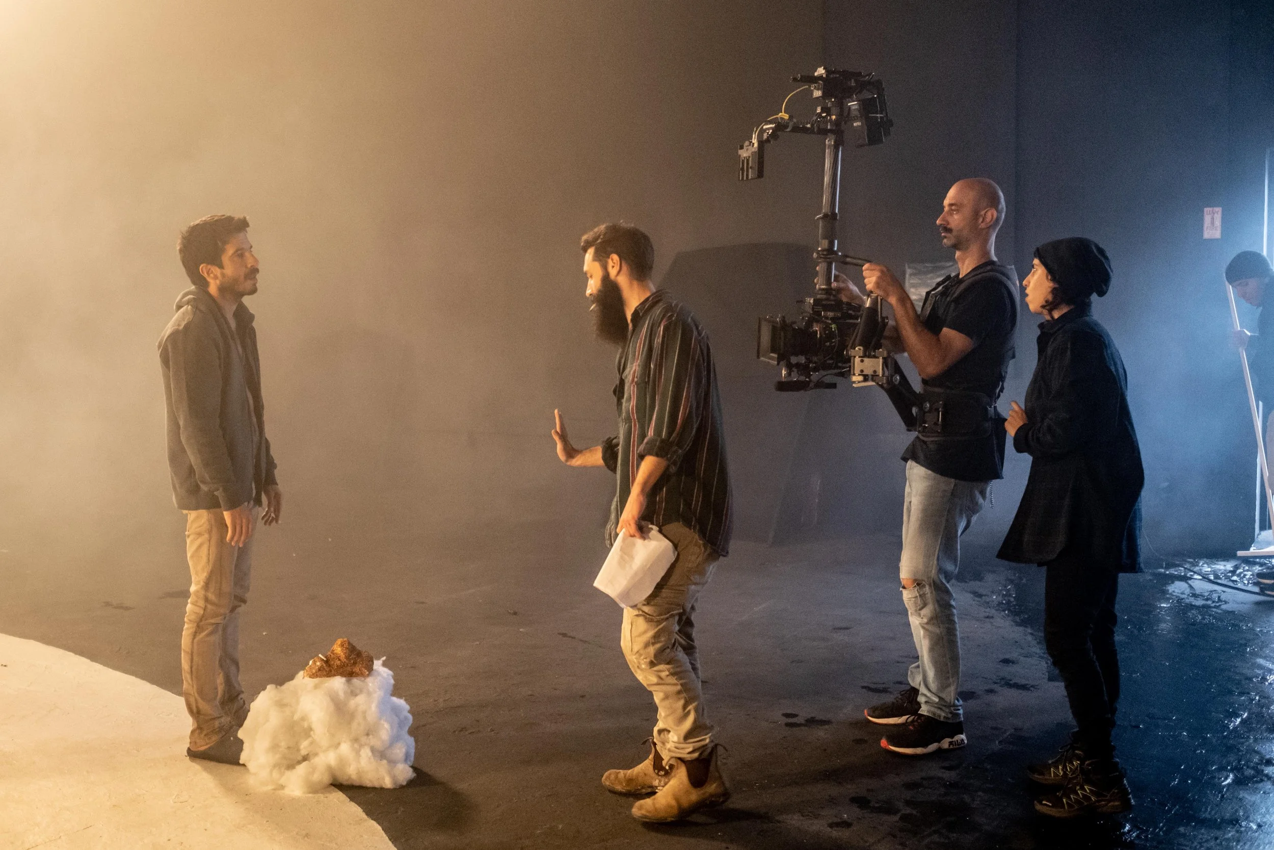 Film set with crew and two actors facing each other, crew operating camera, artificial lighting, and snow on the ground.