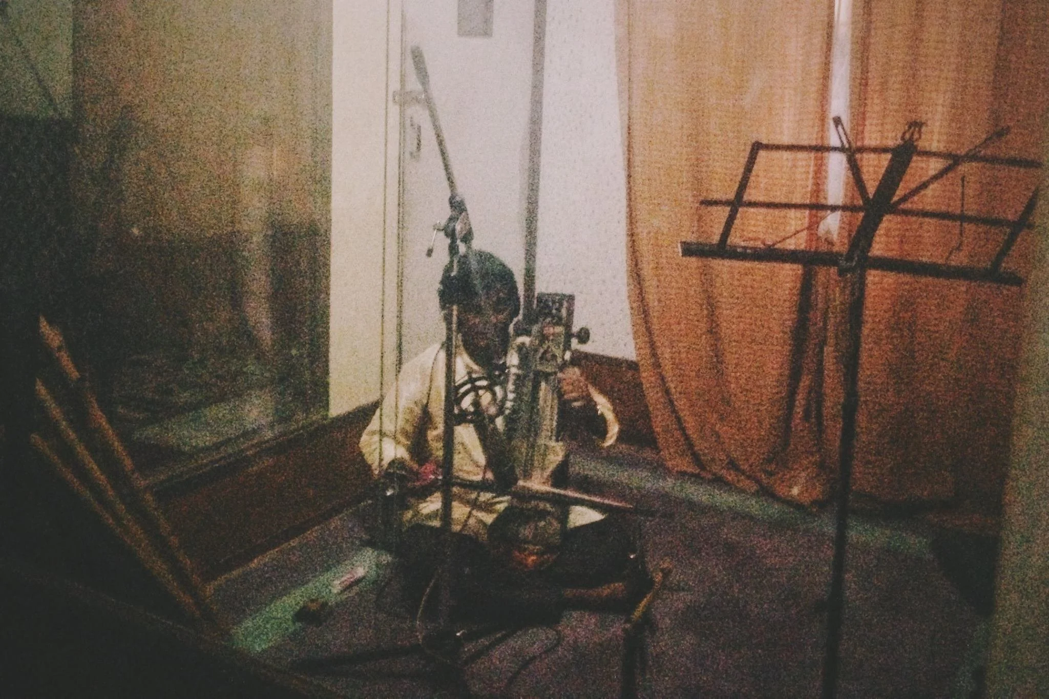 A vintage sewing machine with a piece of fabric, surrounded by various objects including chairs and a wall with a door, in a dimly lit room.