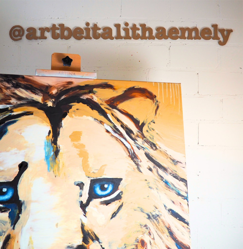 Ein Gemälde eines Löwen mit blauen Augen hängt an einer weißen Wand. Über dem Gemälde ist der Instagram-Handle @artbeitalthaemely sichtbar.