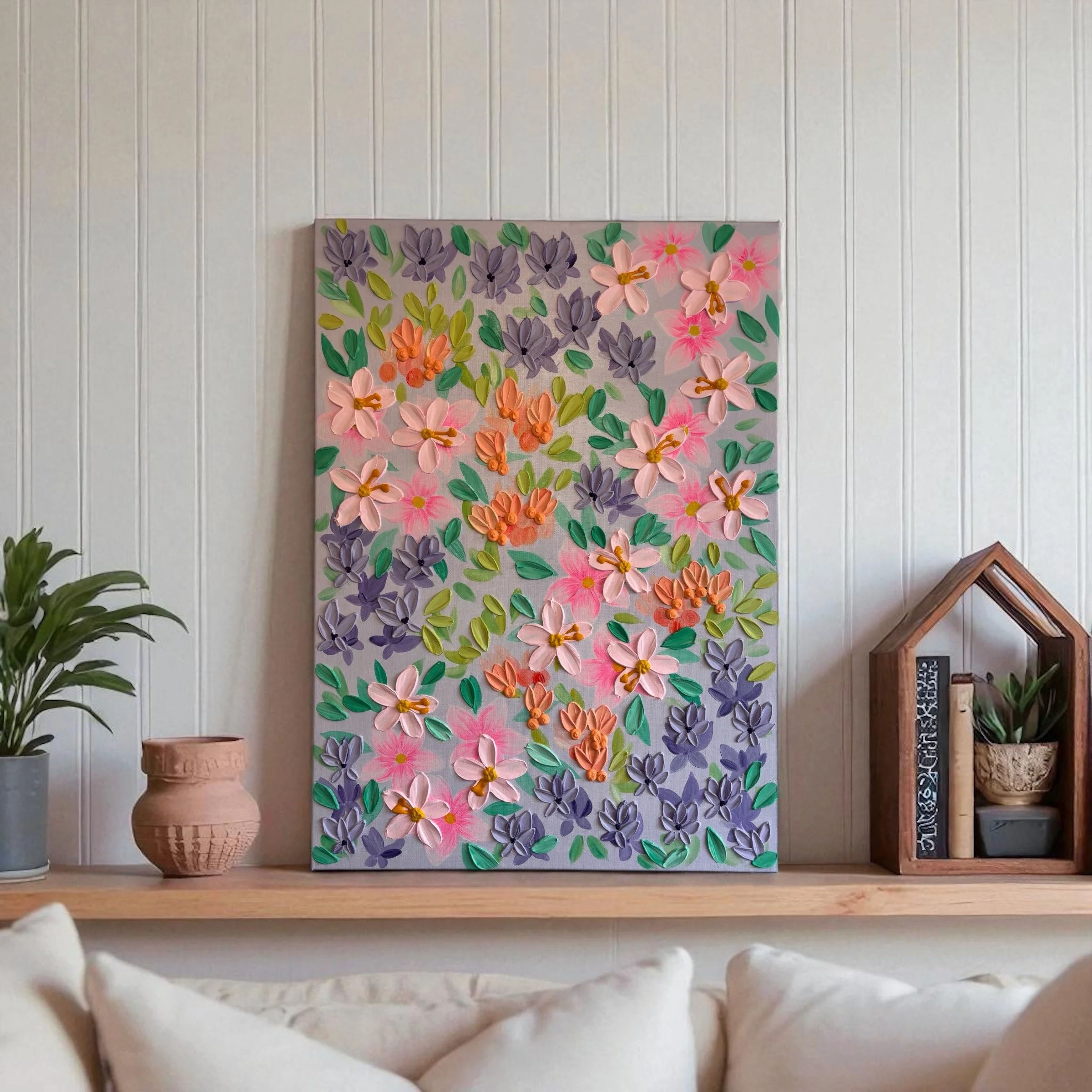 A floral artwork with 3D pink, purple, and orange flowers and green leaves on a gray background, displayed on a wall.