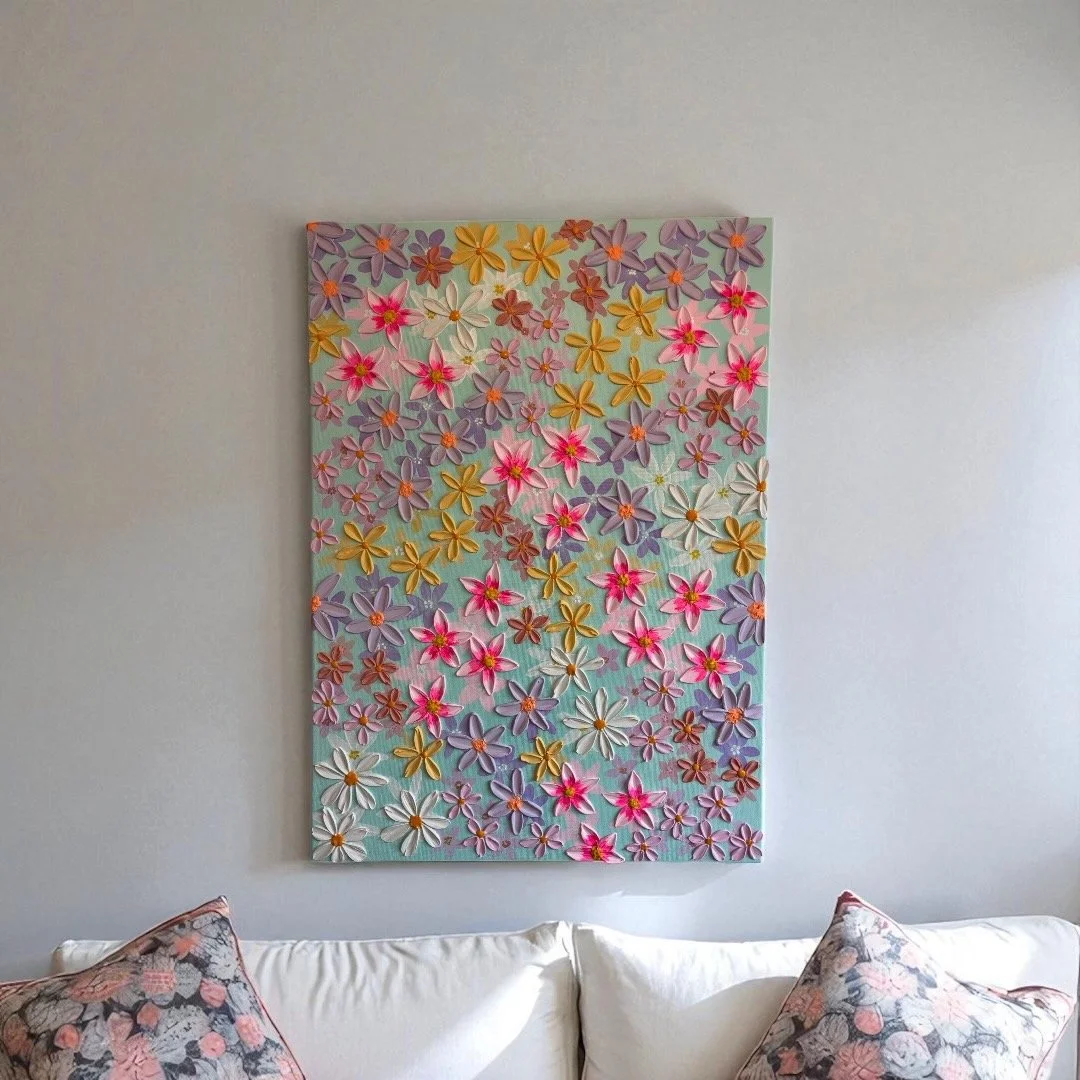 Colorful floral wall art featuring pink, purple, yellow, and white flowers hanging above a white sofa with floral pillows.