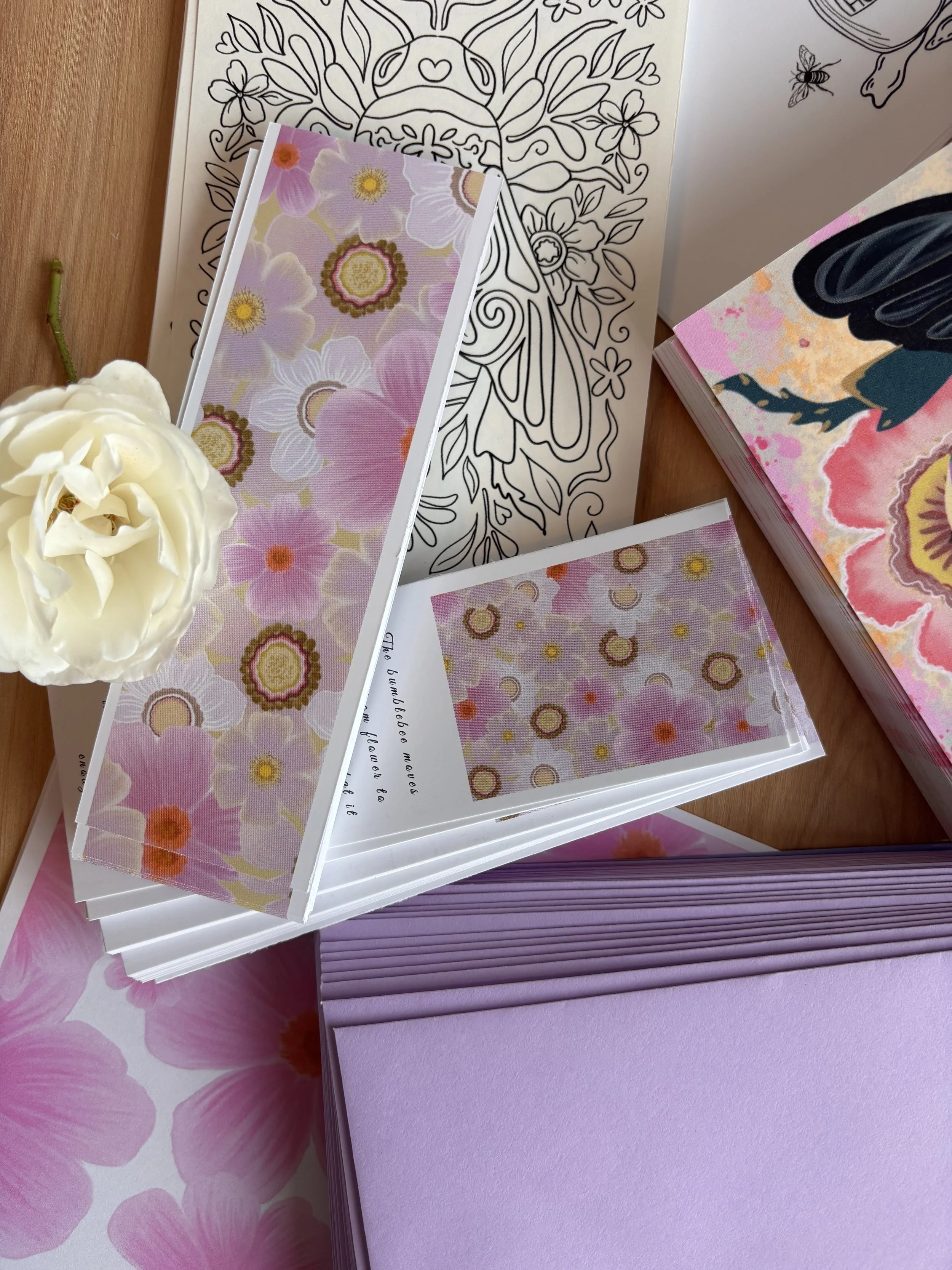 Various printed and patterned papers including floral designs, a black-and-white line drawing, a sheet with text, and a purple textured sheet, with a white flower and a purple book or notebook in the background.
