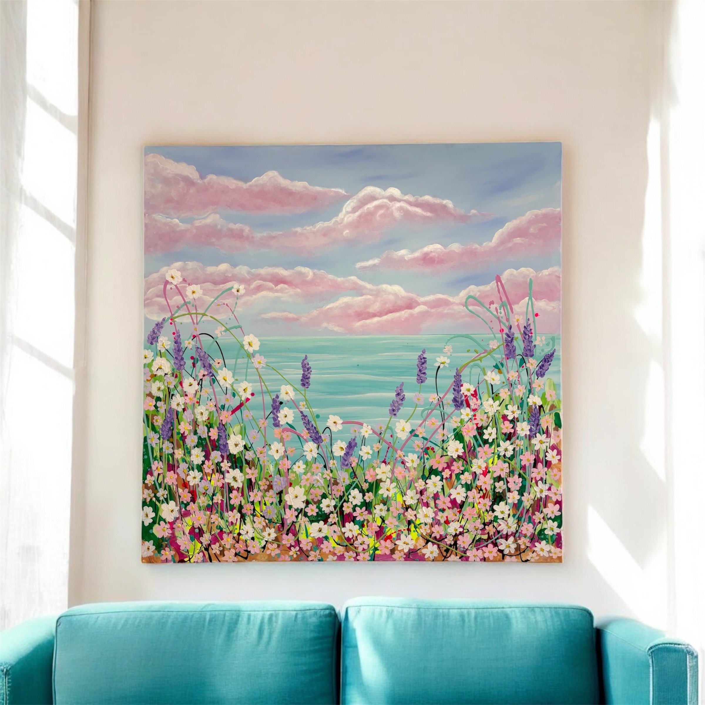 Bright living room featuring a teal sofa positioned below a large colorful landscape painting of clouds in pink and blue hues, with a backdrop of white walls and windows.