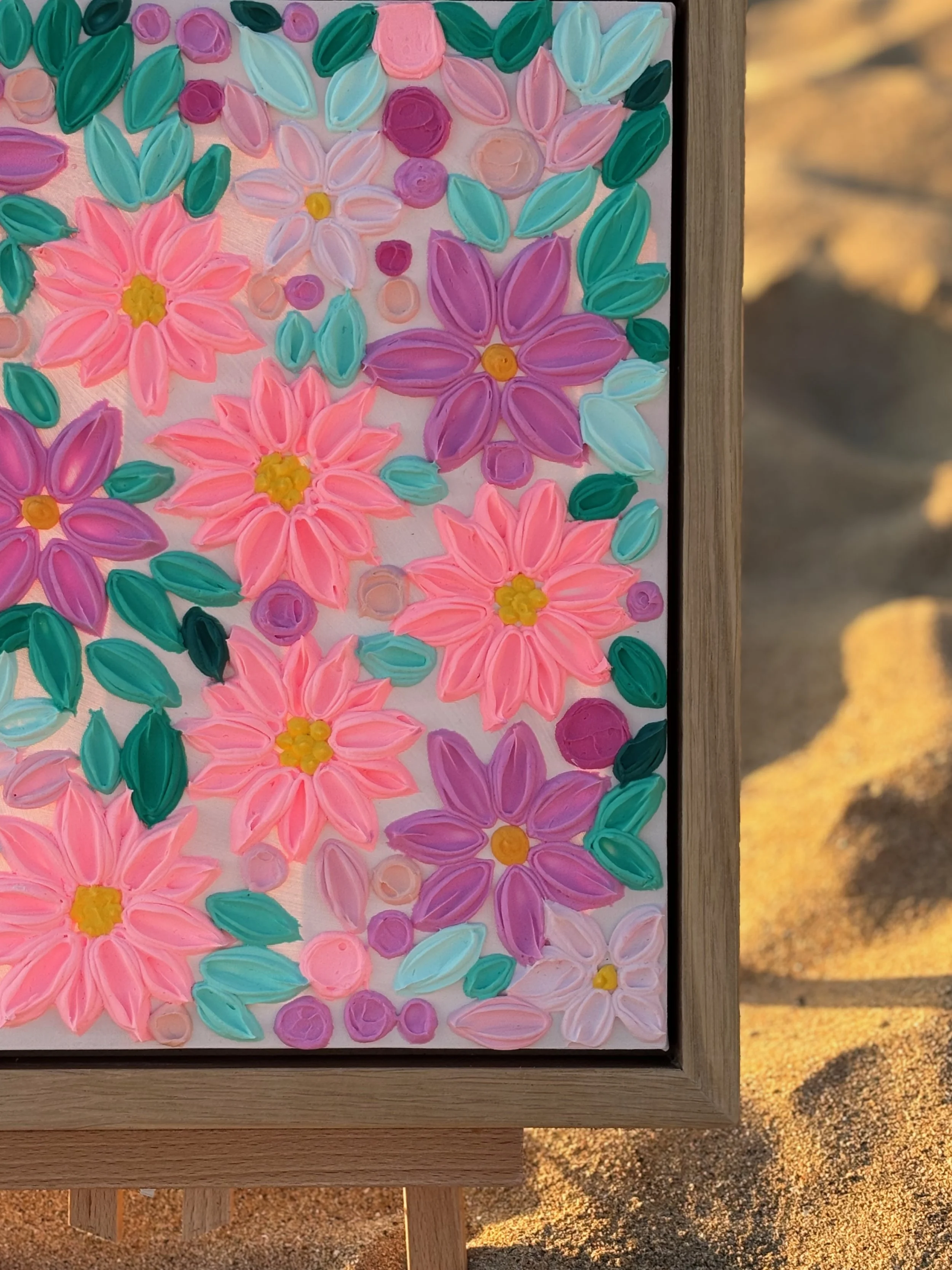 Beach scene with sand, a framed colorful floral painting, and the shadow of a person's head and shoulders on the sand.